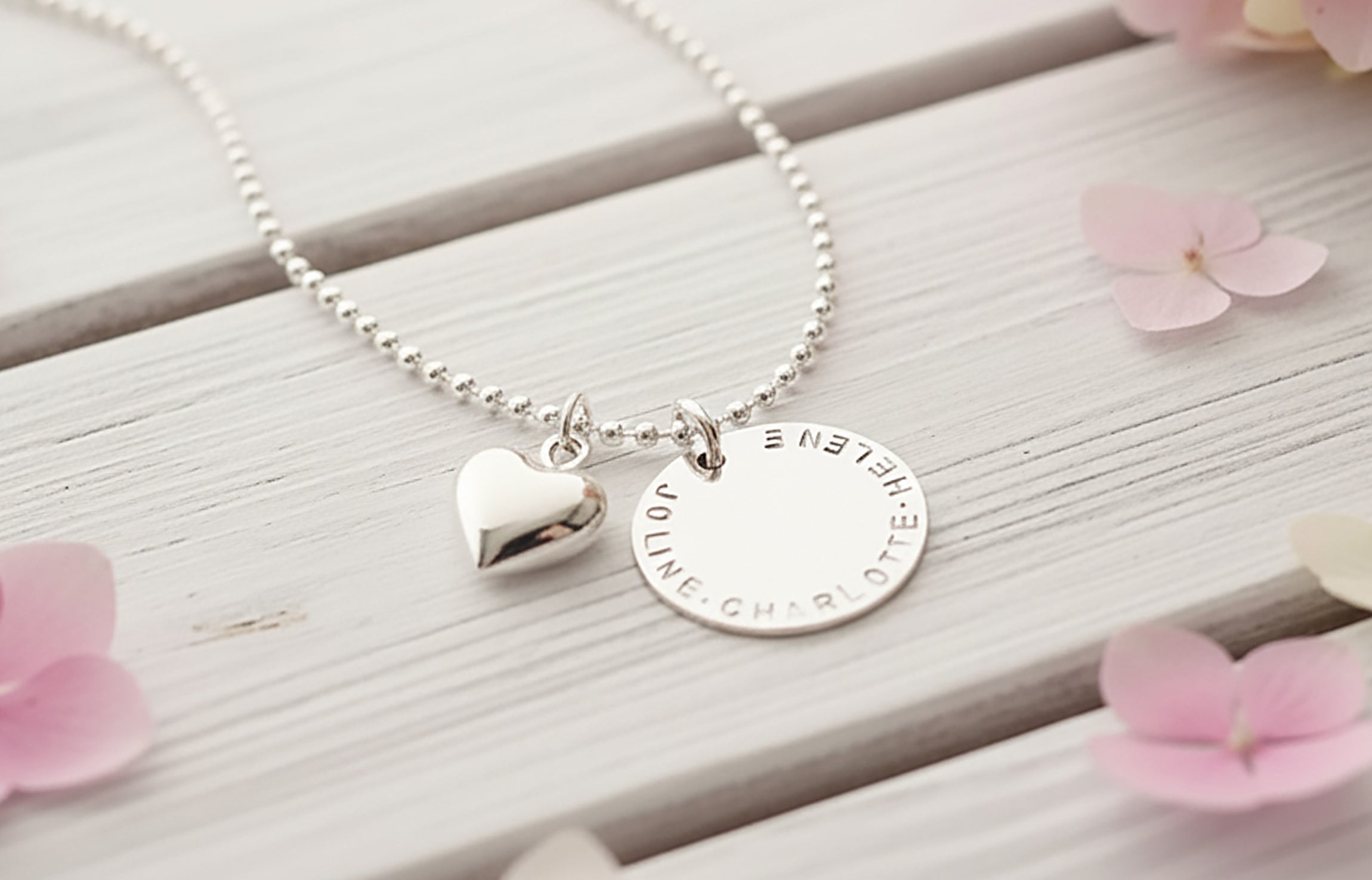 Dein persönliches Unikat: Handgefertigter, gravierbarer Sterling Silberschmuck von Bloomgart, symbolisiert durch einen von Hand gestempelten Namenstaler und ein Herz.