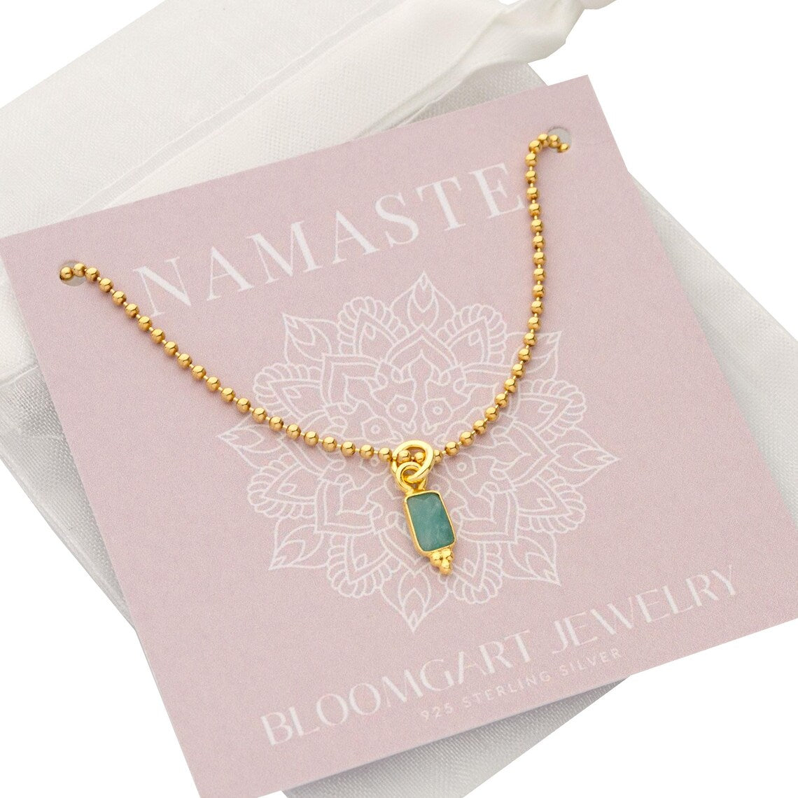 Filigrane goldene Kugelkette mit einem rechteckigen, grün-türkisen Amazonit Anhänger von Bloomgart im weißen Organza-Säckchen.