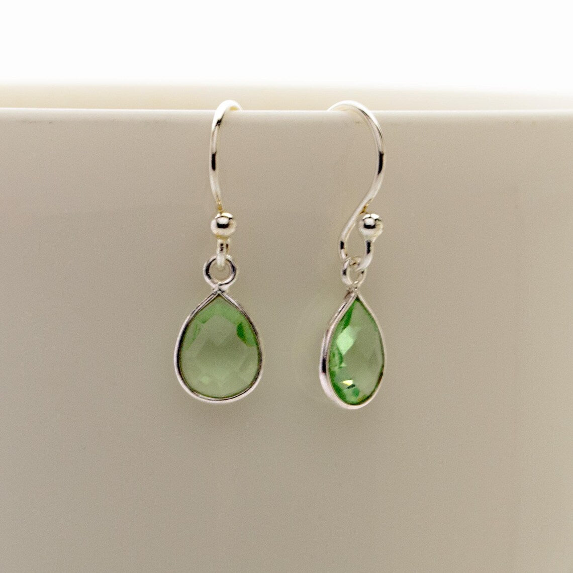 Zierliche Tropfen-Ohrringe mit grünem Amethyst und 925 Sterling Silber Fassung als Makroaufnahme hängend.