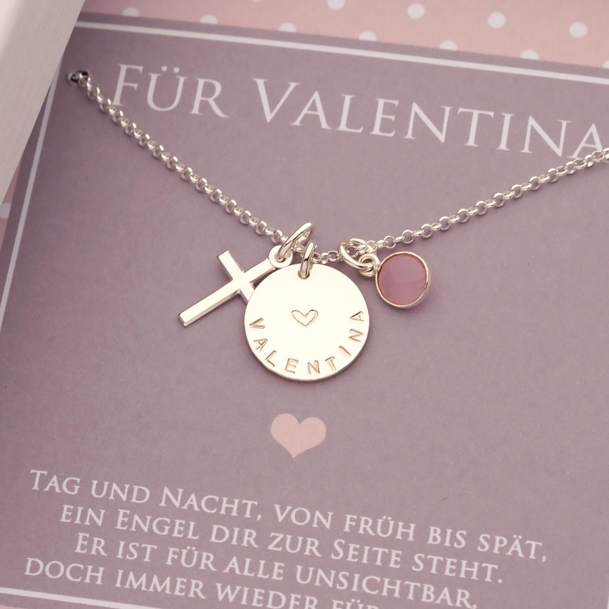 Nahaufnahme der Silberkette mit Namenstaler, hier 'VALENTINA' mit Herz mittig von Hand gestempelt, Kreuz-Anhänger links und Edelstein rechts vom Namen.