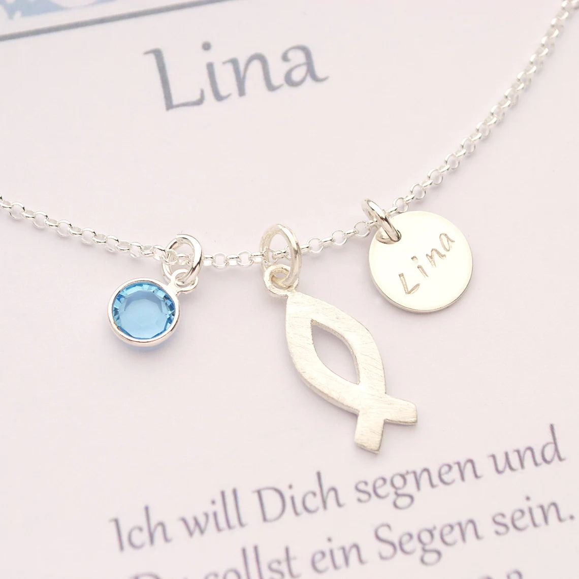 Detailansicht einer Silberkette zur Kommunion mit Ichthys-Fisch Symbol, Monatsstein, hier März (hellblau) und Namenstaler.