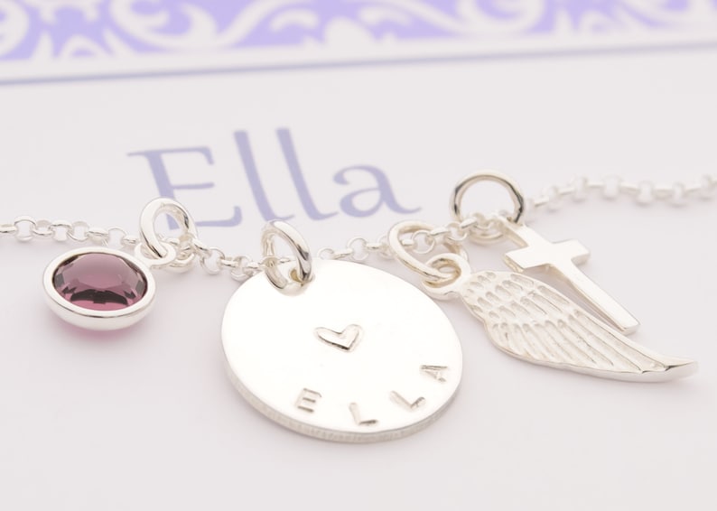 Detailansicht einer zarten Silberkette mit vier Anhängern: lila Amethyst, 15 mm Namenstaler, Engelsflügel und Kreuz aus 925 Sterling Silber.