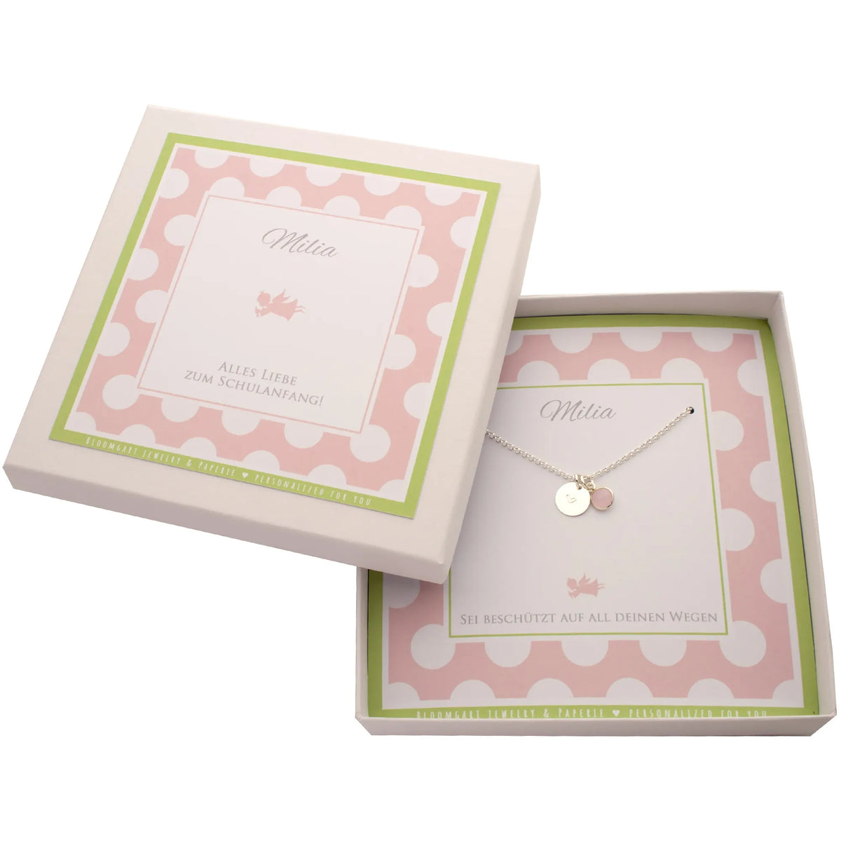 Eine personalisierte, weiße Geschenkbox mit Punktemuster in rosa und hellgrün. Hier für Milia zum Schulanfang mit Silberkette mit graviertem Herz auf einem Silbertaler und Edelstein-Anhänger.