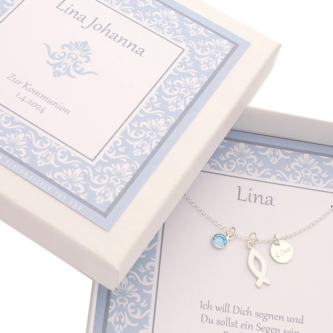Personalisierte blau-weiße Geschenkbox mit edlem Ornamentmuster. Innen liegt eine Silberkette zur Kommunion mit Ichthys-Fisch Symbol, Monatsstein, hier März (hellblau) und Namenstaler.