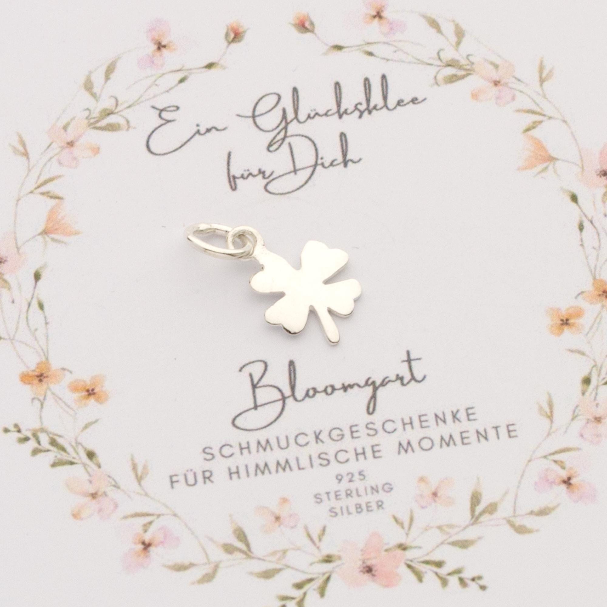 Ein einzigartiger, filigraner Kleeblatt-Anhänger aus 925 Sterling Silber auf einer geblümten Karte präsentiert.