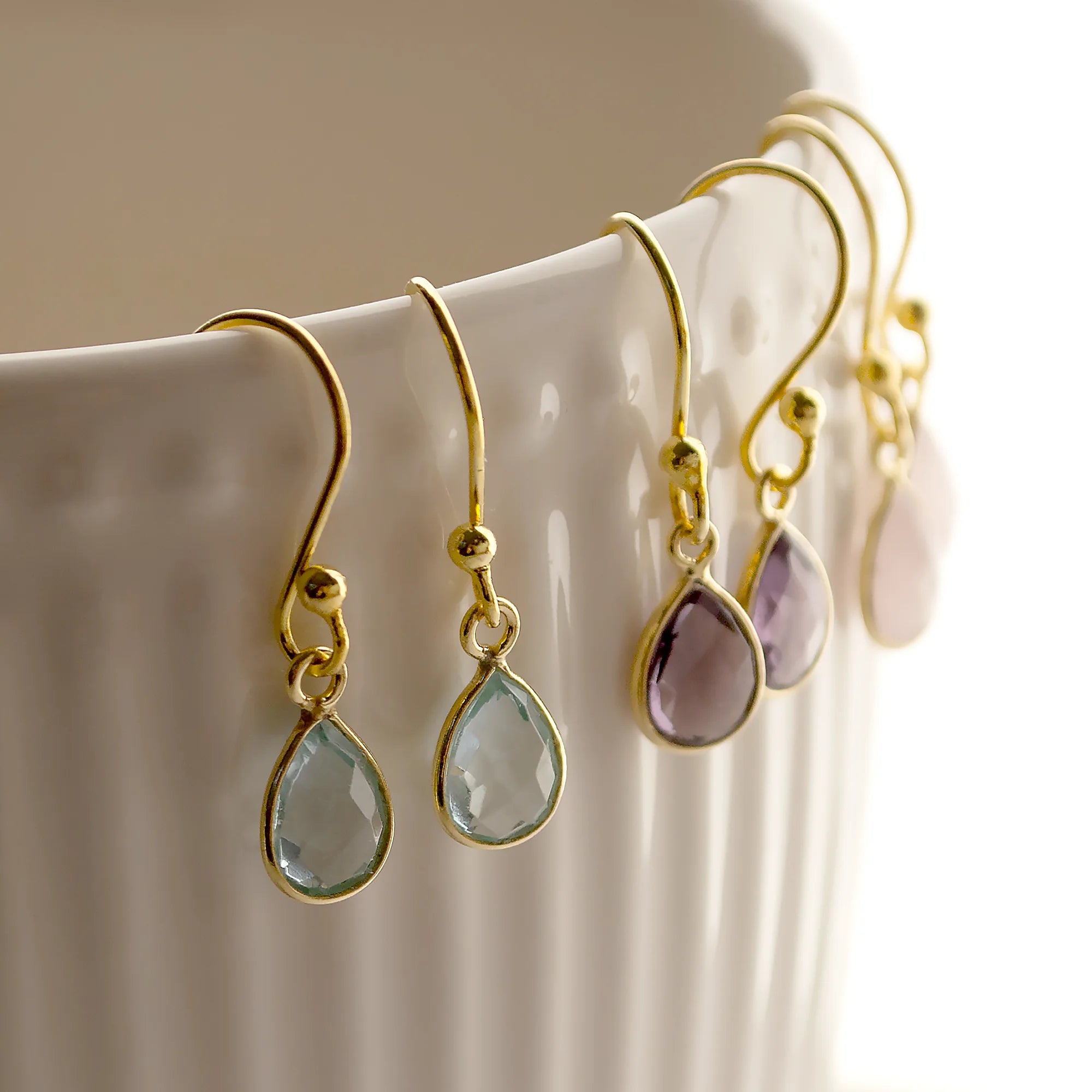 Gold Ohrringe mit Aqua Chalcedon, lila Amethyst und Rosenquarz als Nahaufnahme an einer Porzellantasse fotografiert.