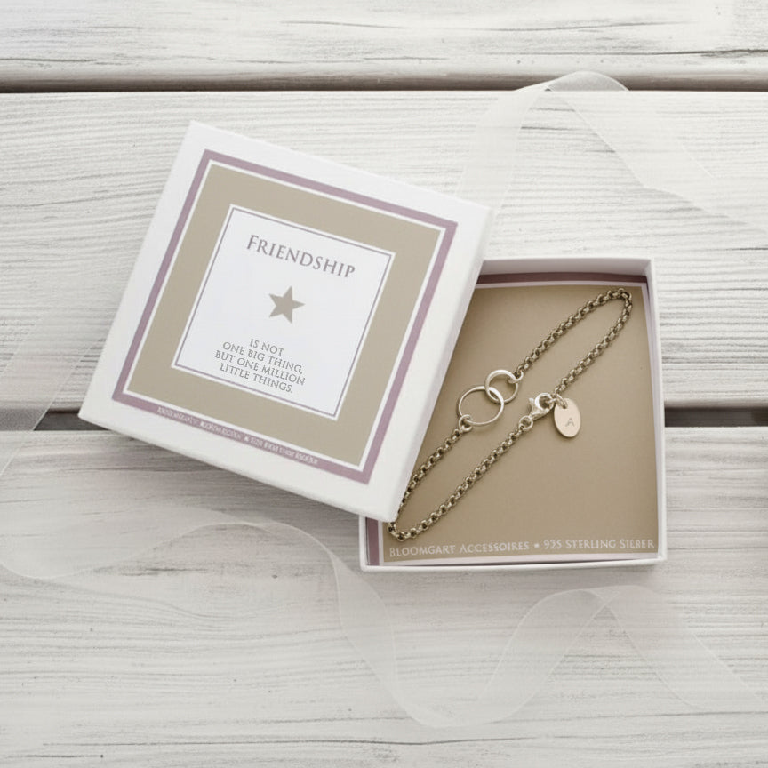 Silberarmband 'verschlungen' mit Gravur-Initial auf einem ovalen Silberplättchen. Das Armband ist zum Verschenken bereit in einer kleinen beige-weißen geschenkbox verpackt. Außen ist der Spruch 'Friendship is not one big thing, but one million little things.'