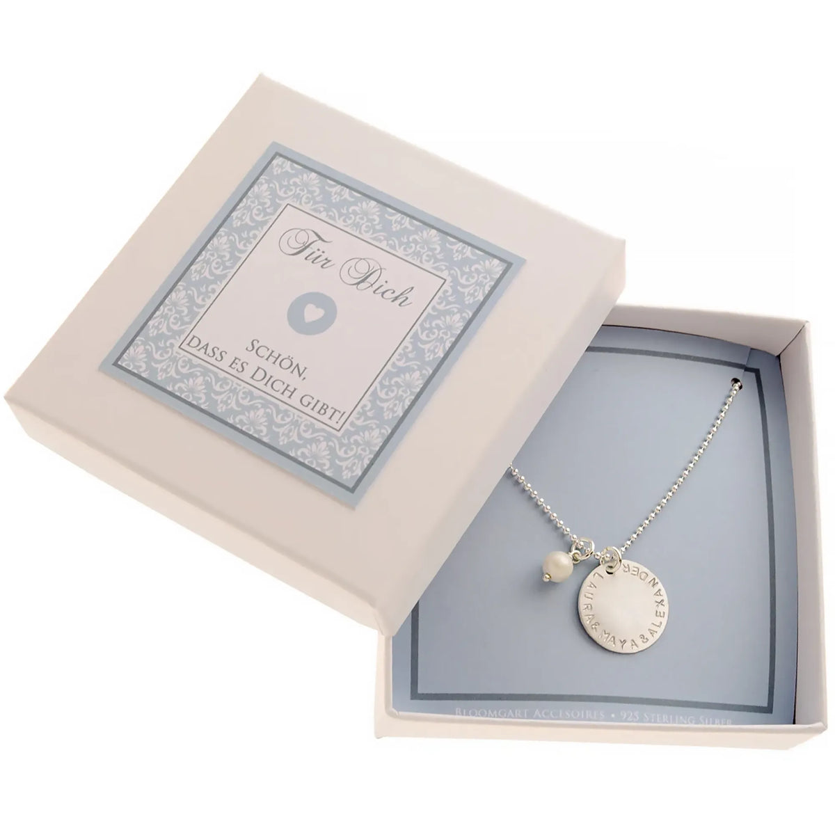 Komplettansicht einer kleinen offenen Geschenkbox mit hellblau-weißem Ornamentmuster. Innen liegt eine 925 Silberkette mit großem Gravur-Plättchen mit der Gravur "LAURA & MAYA & ALEXANDER".