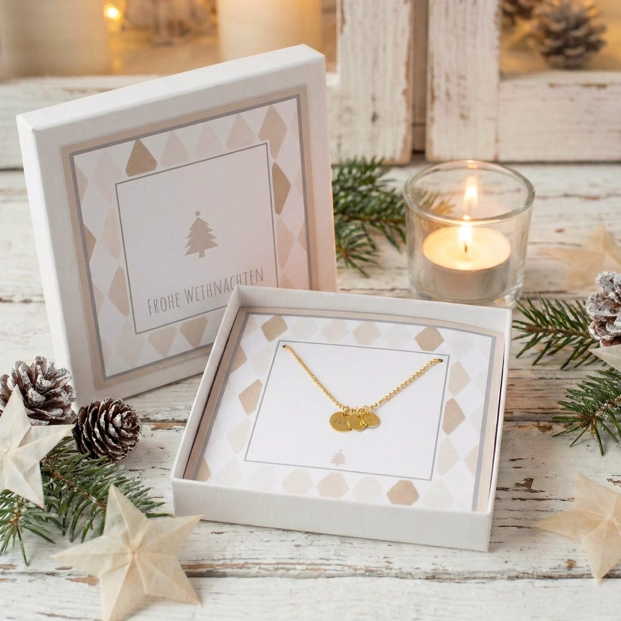 Goldkette mit drei Gravur-Anhängern in einer weihnachtlichen beige-weißen Geschenkbox verpackt. Das Geschenk wird auf einem weihnachtlich dekorierten weißen Holztisch präsentiert.