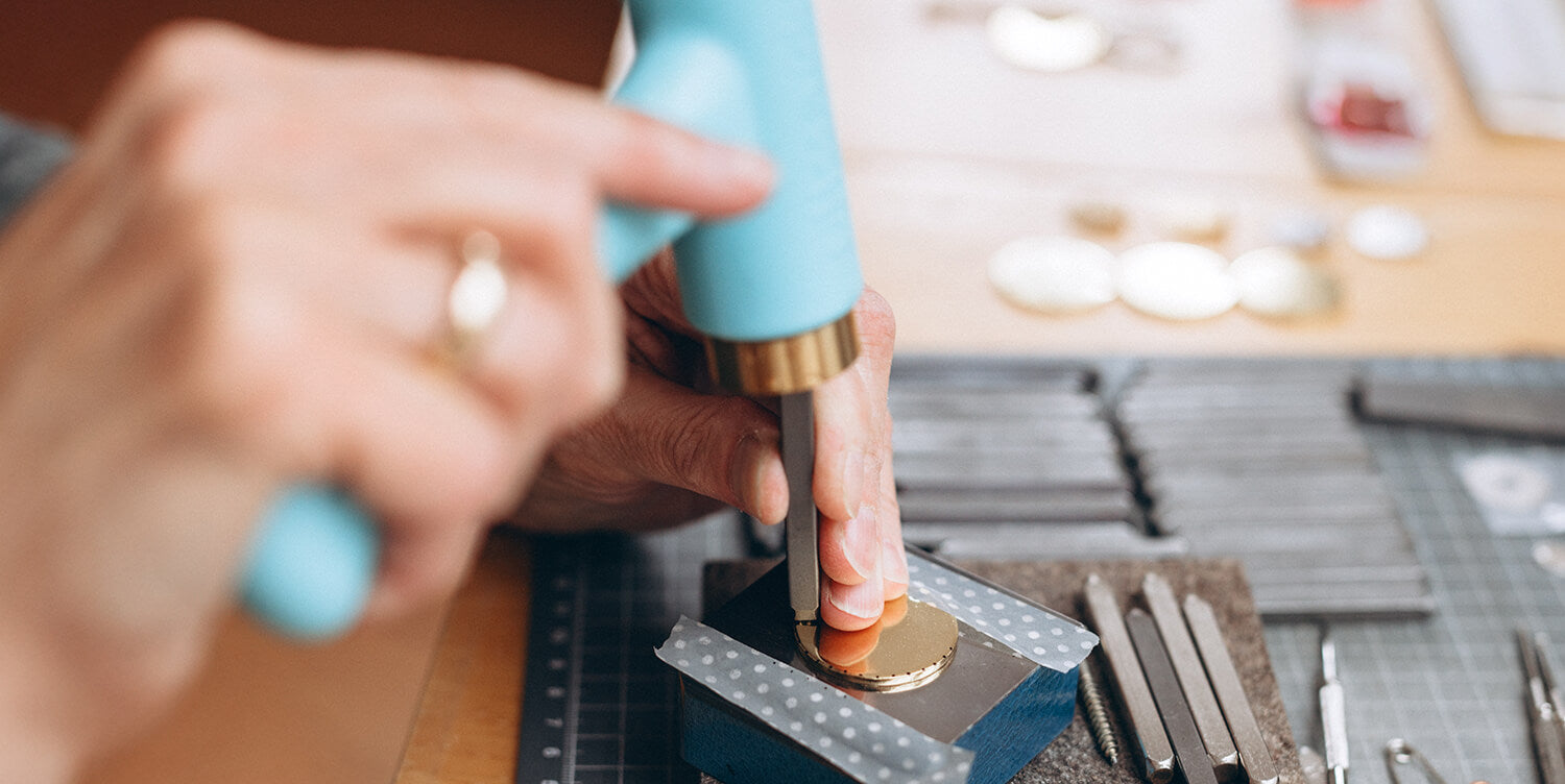 Jeder Buchstabe von Hand gestempelt: Die Designerin prägt mit einem Metallstempel eine persönliche Gravur in einen Silber-Anhänger von Bloomgart.