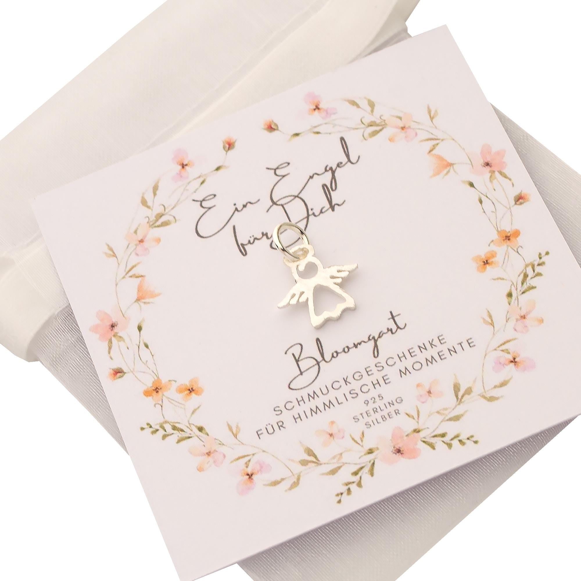 Ein einzigartiger, filigraner Schutzengel-Anhänger aus 925 Sterling Silber auf einer geblümten Karte präsentiert und im Organza-Säckchen verpackt.