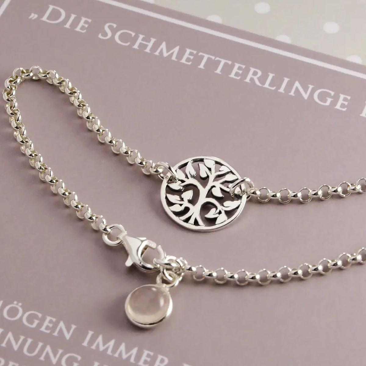Detailaufnahme eines Armbands aus 925 Sterling Silber mit rundem Lebensbaum-Verbinder und Rosenquarz-Anhänger auf einer beige-braunen Hochzeitskarte.