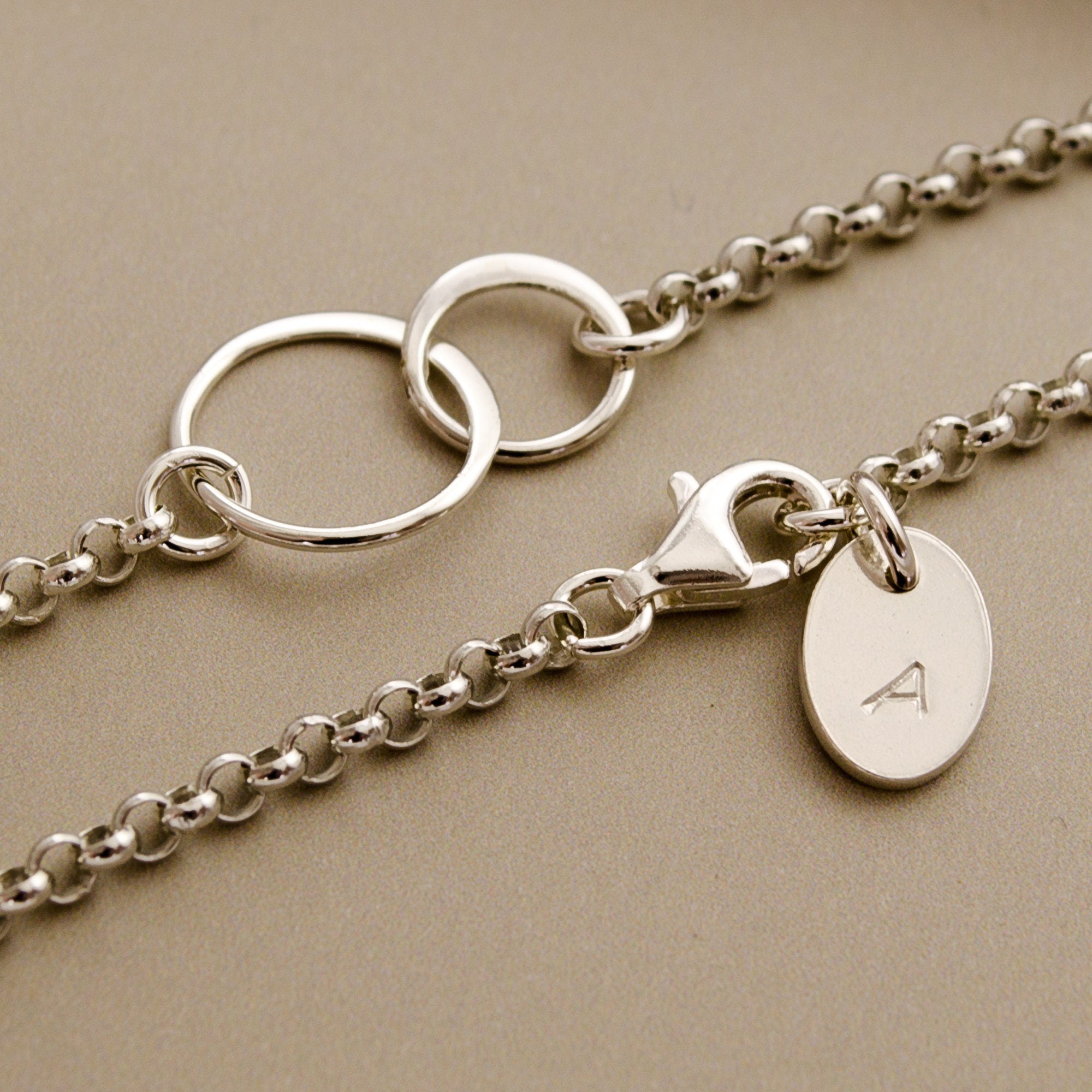 Detailansicht des 925 Silber Gliederarmbandes mit zwei verschlungen Ringen und Initial-Gravurplättchen am Verschluss.