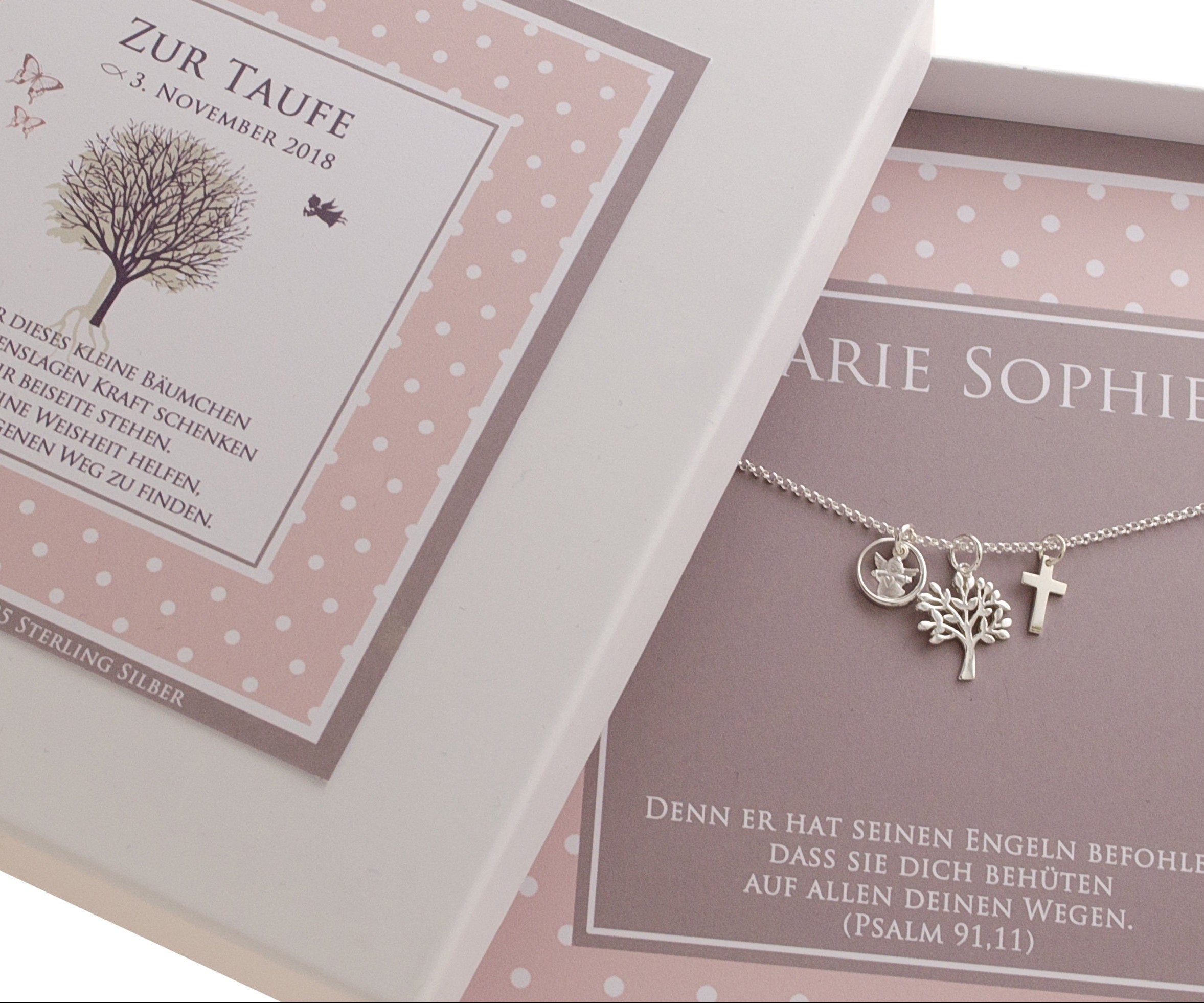 angeschnittene Darstellung einer personalisierten Geschenkbox im rosa-taupe Pünktchen-Design zur Taufe. Innenliegend befindet sich eine zarte Gliederkette mit Engel im Ring, Lebensbuam und Kreuz.