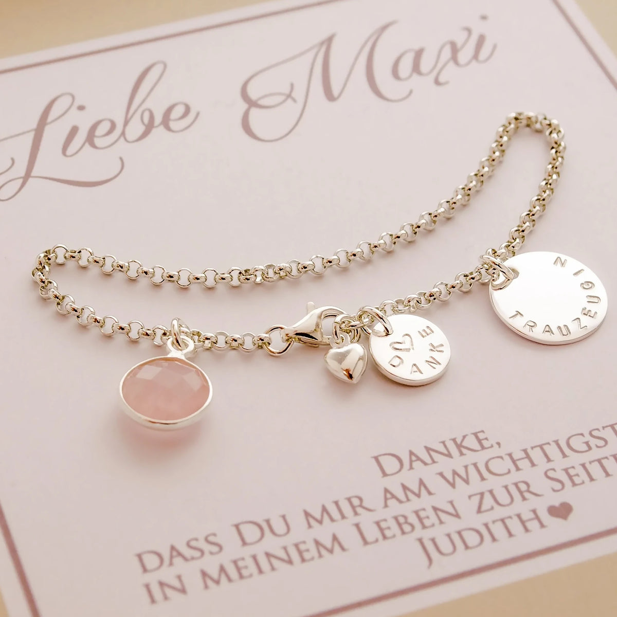 Zartes 925 Silberarmband für die Trauzeugin mit Rosenquarz, kleinem Gravur-Taler mit 'Danke' und einem Herz mittig gestempelt und einem großen von Hand gestempelten Anhänger mit Gravur 'Trauzeugin'. Am Ende des Armbandes ist ein kleines bauchiges Herz befestigt. Das Armband wird in einer süßen personalisierten Geschenkbox in beige-weiß präsentiert.