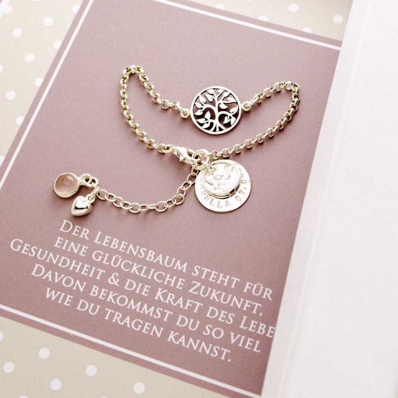 Personalisiertes Silberarmband mit Lebensbaum, Rosenquarz und Engel. Ein großer Namenstaler ist von Hand mit Namen und Datum gestempelt.