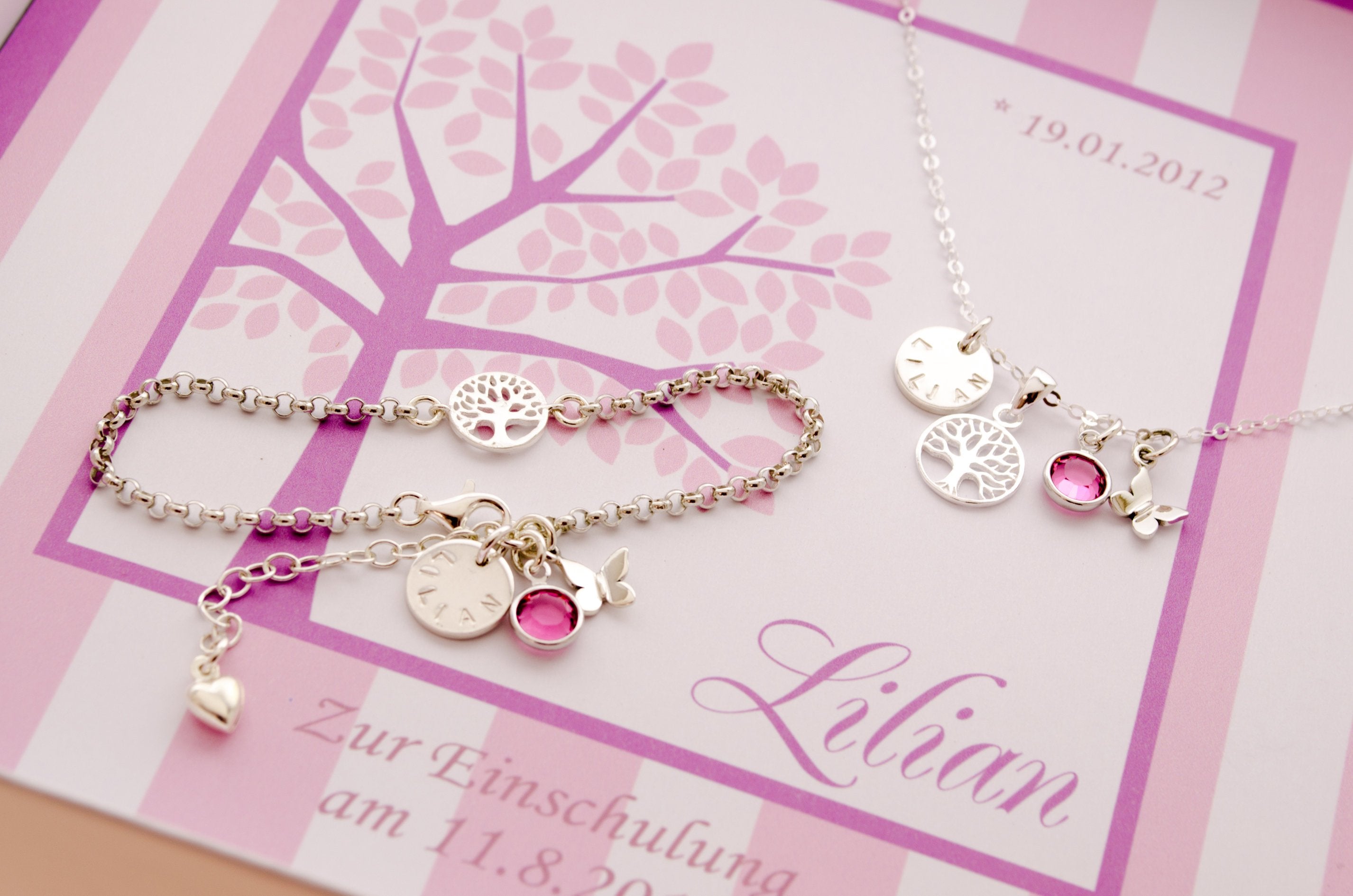 Detailansicht der Geschenkbox mit stilisiertem Lebensbaum in rosa-pink-weiß und filigranem Schmuck-Set aus Silberkette und Silberarmband mit Namenstaler, rundem Lebensbaum, Geburtsstein und Schmetterling.