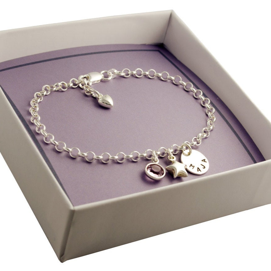 Verstellbares Gliederarmband mit Namenstaler, Glücksstern und Geburtsstein in Juni-Farbe in einer offenen handgefertigten weißen Geschenkbox präsentiert.