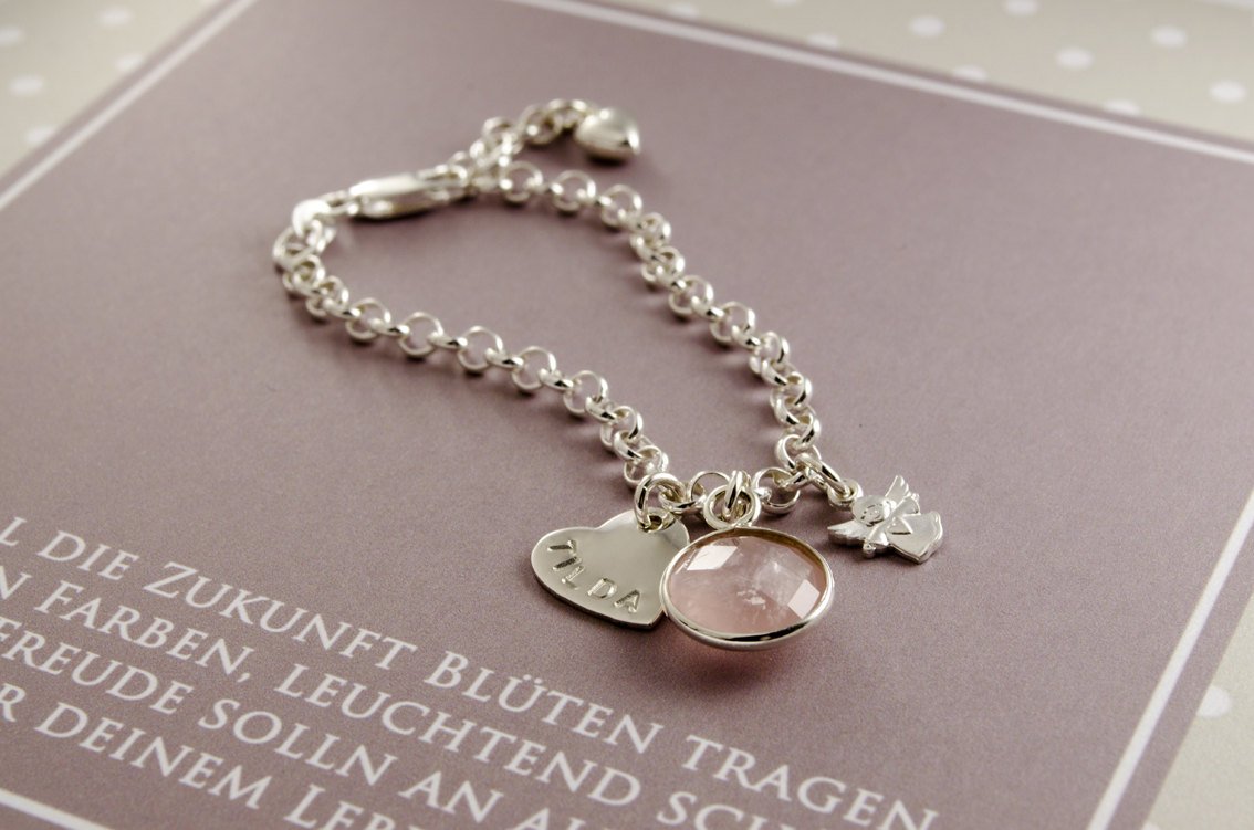 Detailansicht eines sehr süßen Taufarmbandes mit Gravur-Herz, Engel und Edelstein-Anhänger, hier ein Rosenquarz. Das Armband liegt in einer personalisierten Geschenkbox in weiß-beige-braun Tönen im Pünktchen Design.