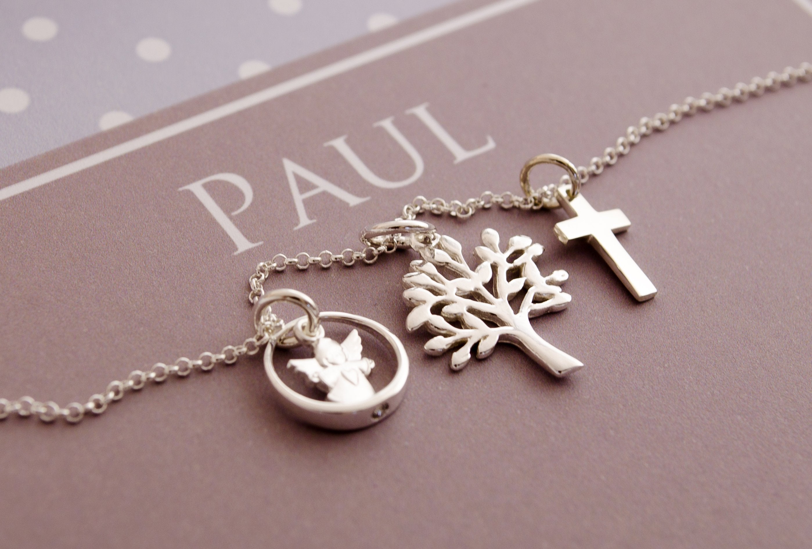 Detailansicht einer filigranen  Silberkette mit Schutzengel, Kreuz und Lebensbaum in einer personalisierten Geschenkbox mit Pünktchen-Design in hellblau-grau-weiß.