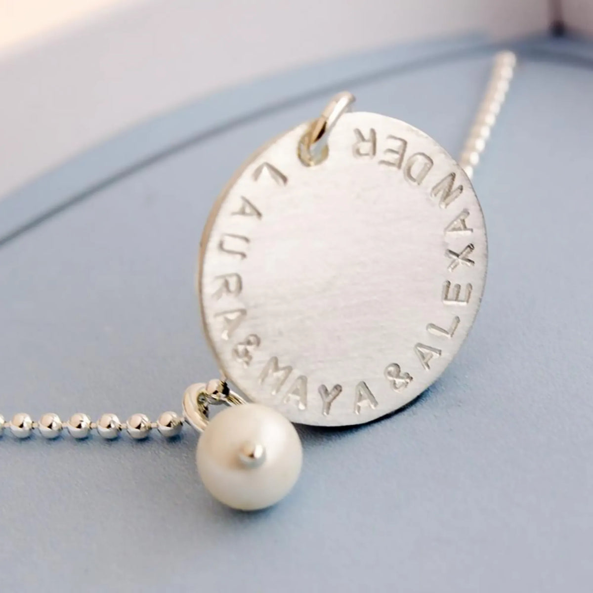 Detailansicht einer 925 Silber Kugelkette mit 18 mm Gravur-Plättchen mit der Gravur "LAURA & MAYA & ALEXANDER" und weißer Süßwasser-Perle.