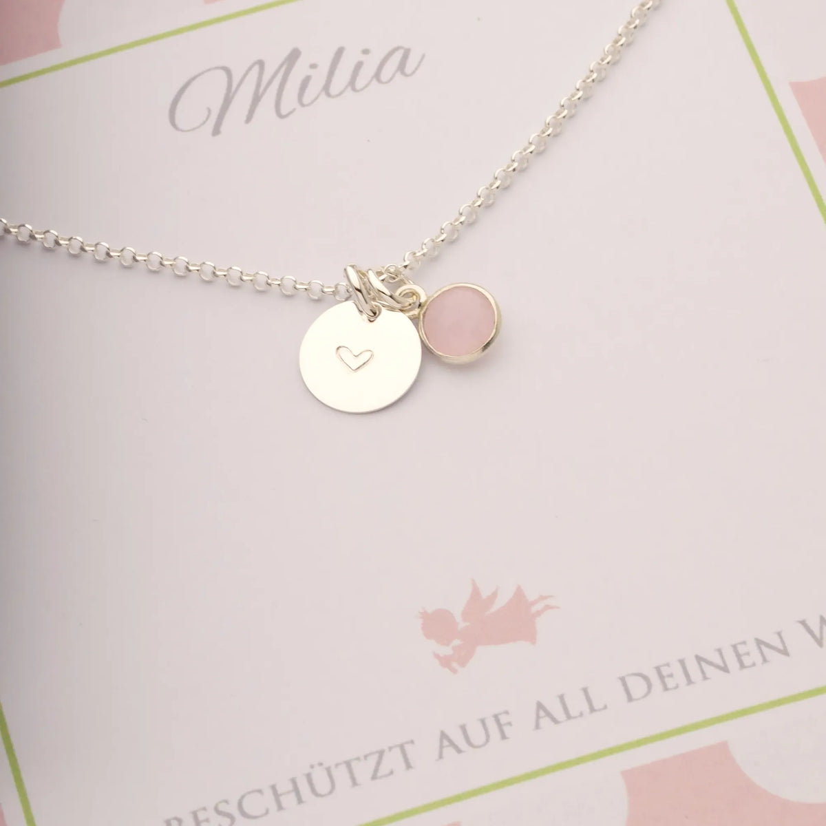 Eine personalisierte, weiße Geschenkbox mit Punktemuster in rosa-hellgrün. Ein Geschenk für Milia zur Einschulung. Innen liegt eine Silberkette mit graviertem Silbertaler und Rosenquarz.