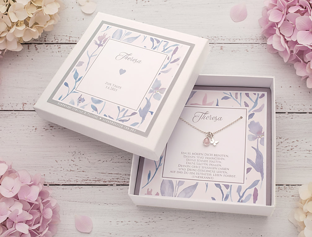Personalisierte 925 Silberkette für "Theresa" mit Schmetterling-Anhänger und rosa Rosenquarz-Tropfen, präsentiert in einer floralen Geschenkbox auf hellem Holzhintergrund mit zarten Blüten. Ein liebevolles Erinnerungsstück für besondere Anlässe wie hier die Taufe.
