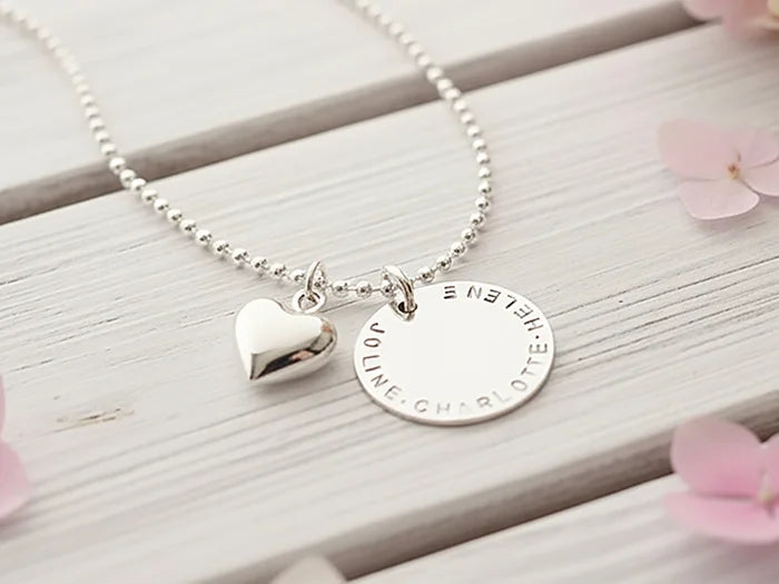Dein persönliches Unikat: Handgefertigter, gravierbarer Sterling Silberschmuck von Bloomgart, symbolisiert durch einen von Hand gestempelten Namenstaler und ein Herz.