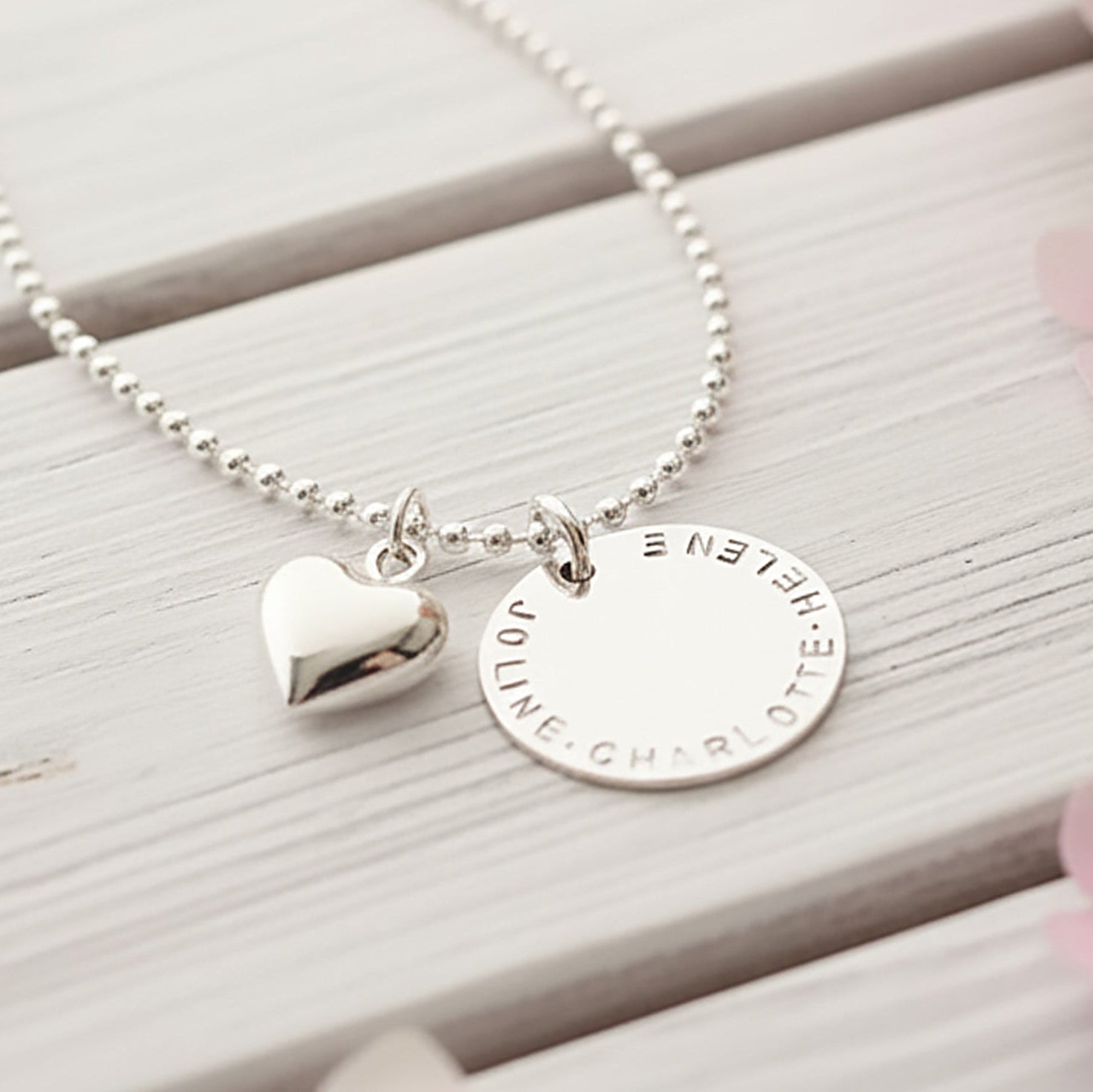 Dein persönliches Unikat: Handgefertigter, gravierbarer Sterling Silberschmuck von Bloomgart, symbolisiert durch einen von Hand gestempelten Namenstaler und ein Herz.