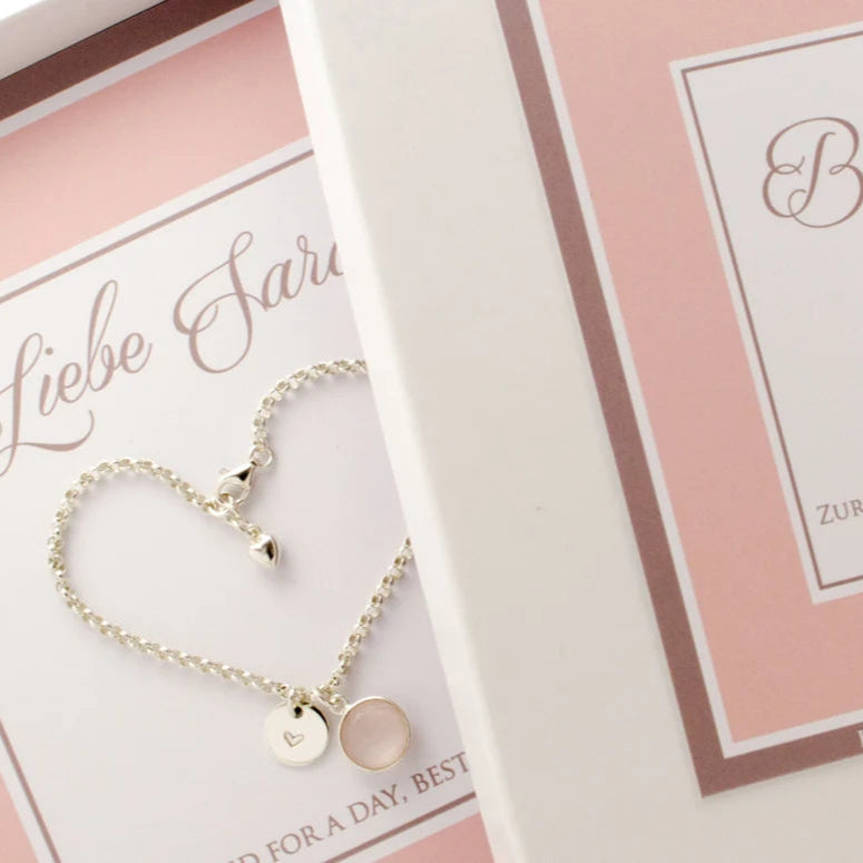 Süßes Geschenk für deine Trauzeugin: ein 925 SIlber Gliederarmband mit rundem Rosenquarz-Anhänger in Silber gefasst und einem rundem Silberplättchen mit handgestempeltem Herz, präsentiert in einer personalisierten weiß-rosa Geschenkbox.