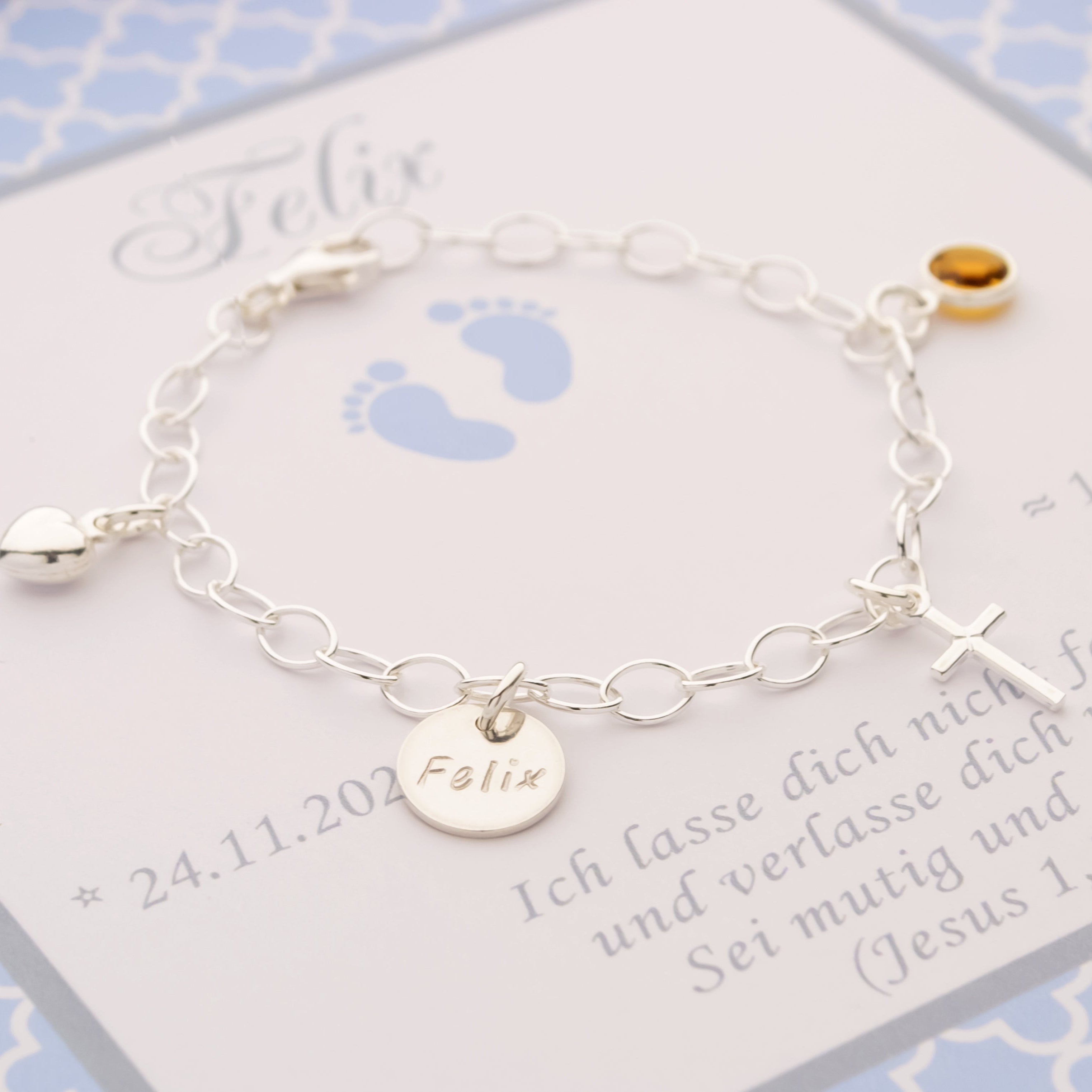 Personalisiertes Taufarmband "Felix" aus 925 Silber mit kleinen Füßchen-Symbolen, Namensgravur und einem gelben Geburtsstein in einer blauen Geschenkbox.