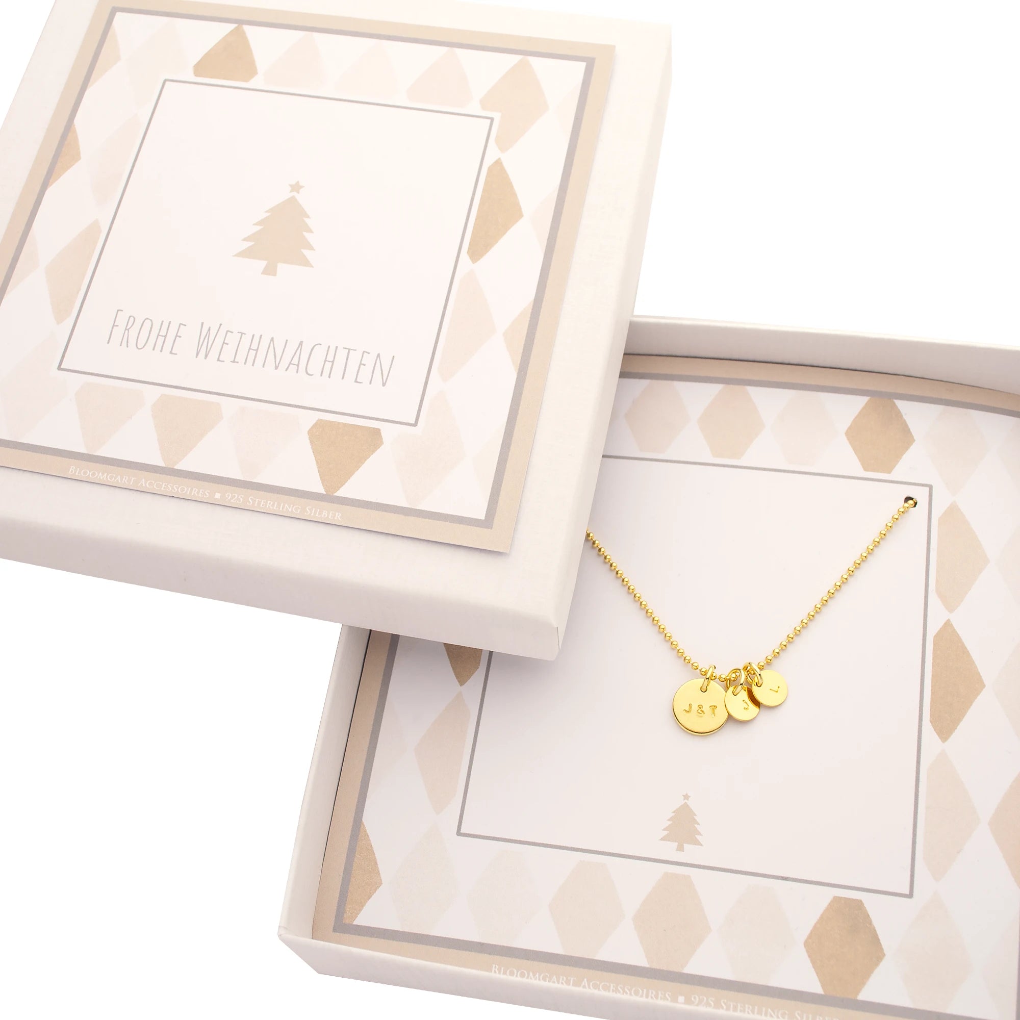 Goldkette mit drei gravierten Initial-Plättchen (J&T, J, L) in einer beige-weißen Geschenkbox mit stilisiertem Tannenbaum und Aufdruck "FROHE WEIHNACHTEN".