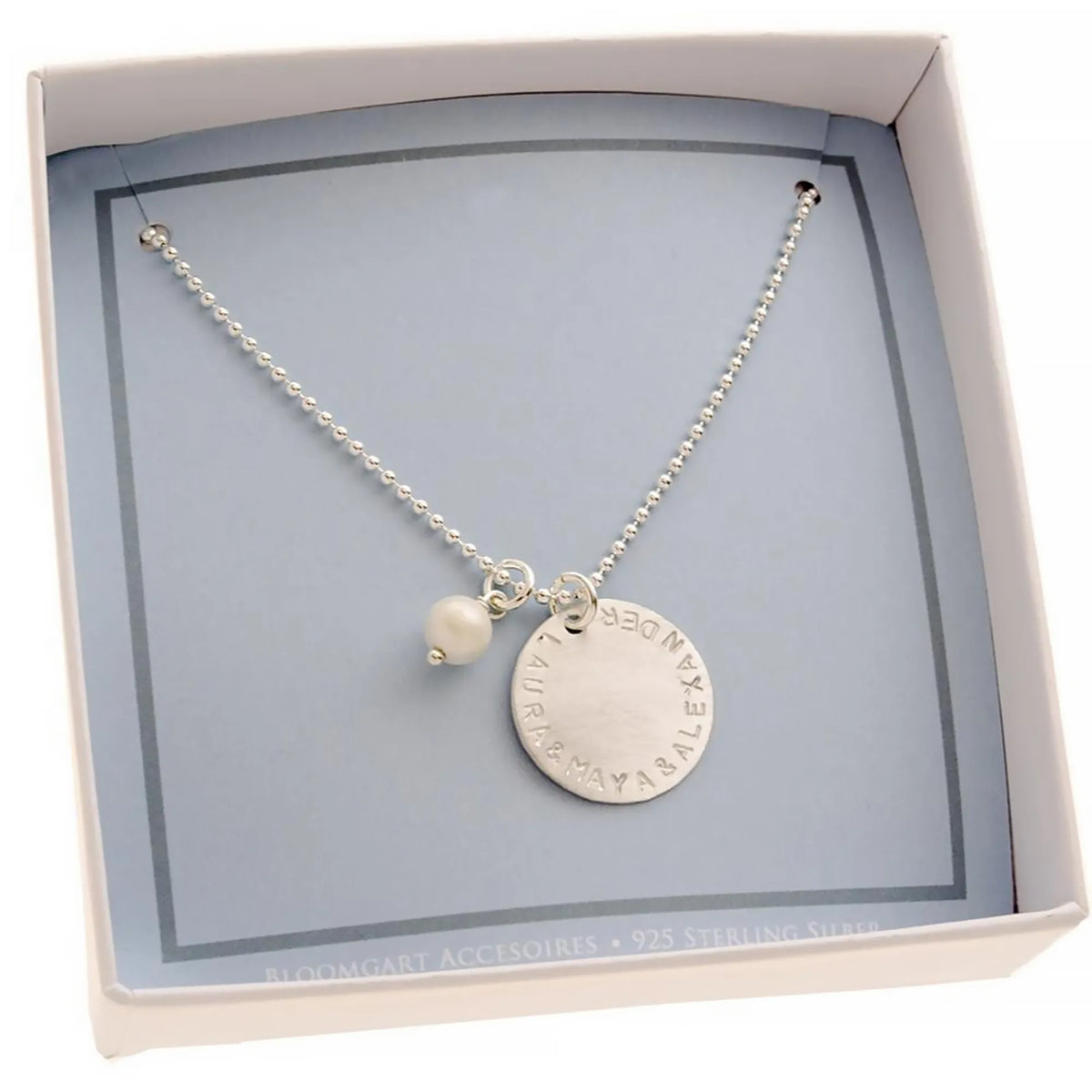 Innenansicht einer kleinen offenen Geschenkbox in hellblau-weiß. Innen liegt eine 925 Silberkette mit großem Gravur-Plättchen mit der Gravur "LAURA & MAYA & ALEXANDER" und weißer Süßwasserperle.