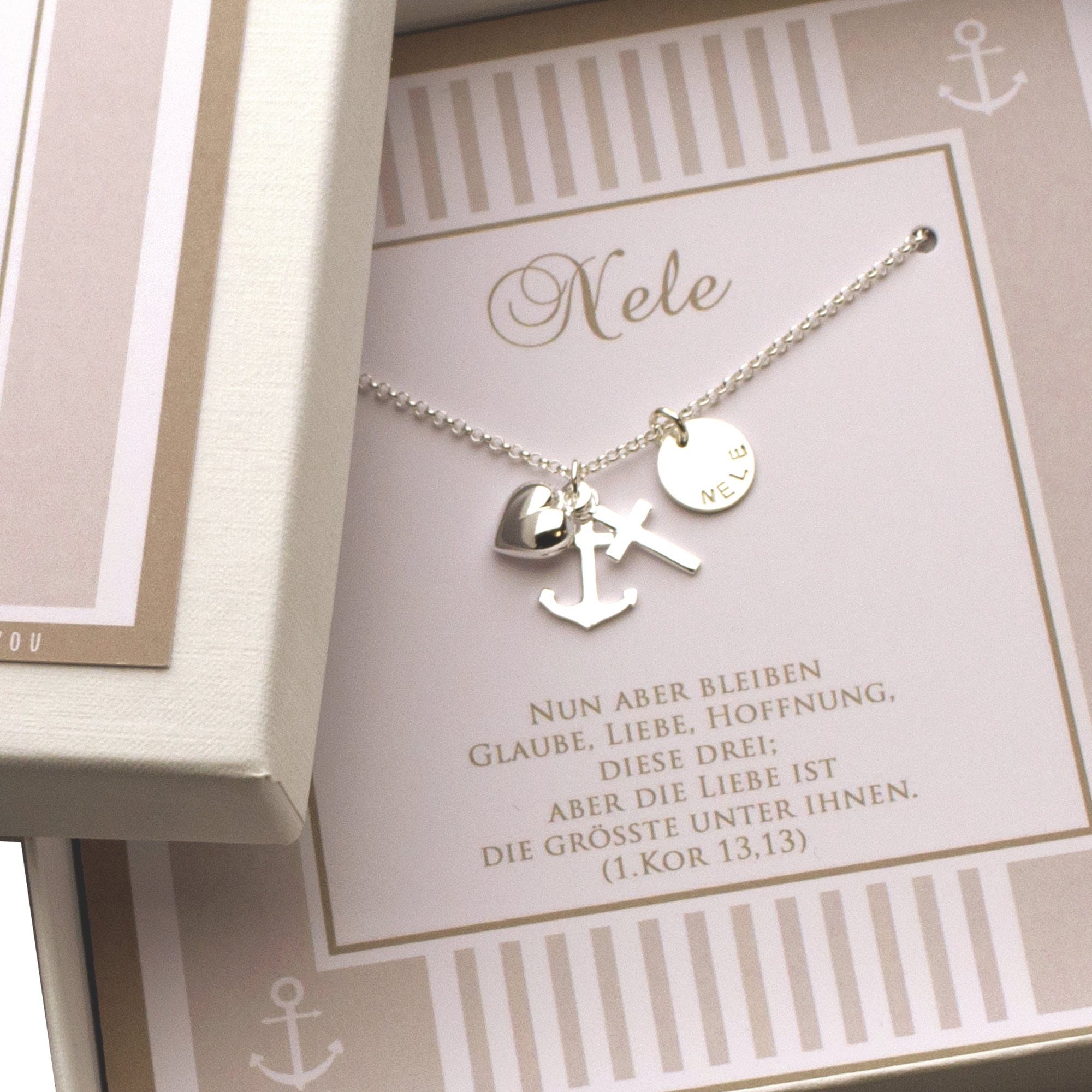 Personalisierte Halskette aus 925 Sterling Silber mit Anhängern für Glaube (Kreuz), Liebe (Herz) und Hoffnung (Anker) sowie einem Gravurplättchen mit dem Namen "Nele". Die Kette liegt in einer Geschenkbox auf einer Karte mit dem Spruch aus 1. Korinther 13,13. Handgemacht von Bloomgart.