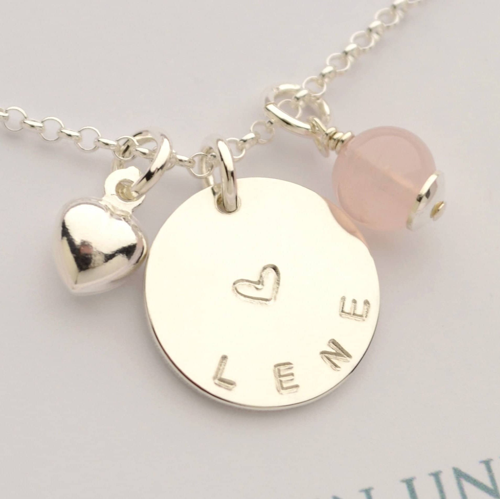 Personalisierte Halskette aus 925 Silber mit handgestempeltem Namen 'Lene', einem Herz-Symbol, einem Herz-Anhänger und einer Rosenquarz-Perle. Handgemachter Schmuck von Bloomgart als Geschenk.
