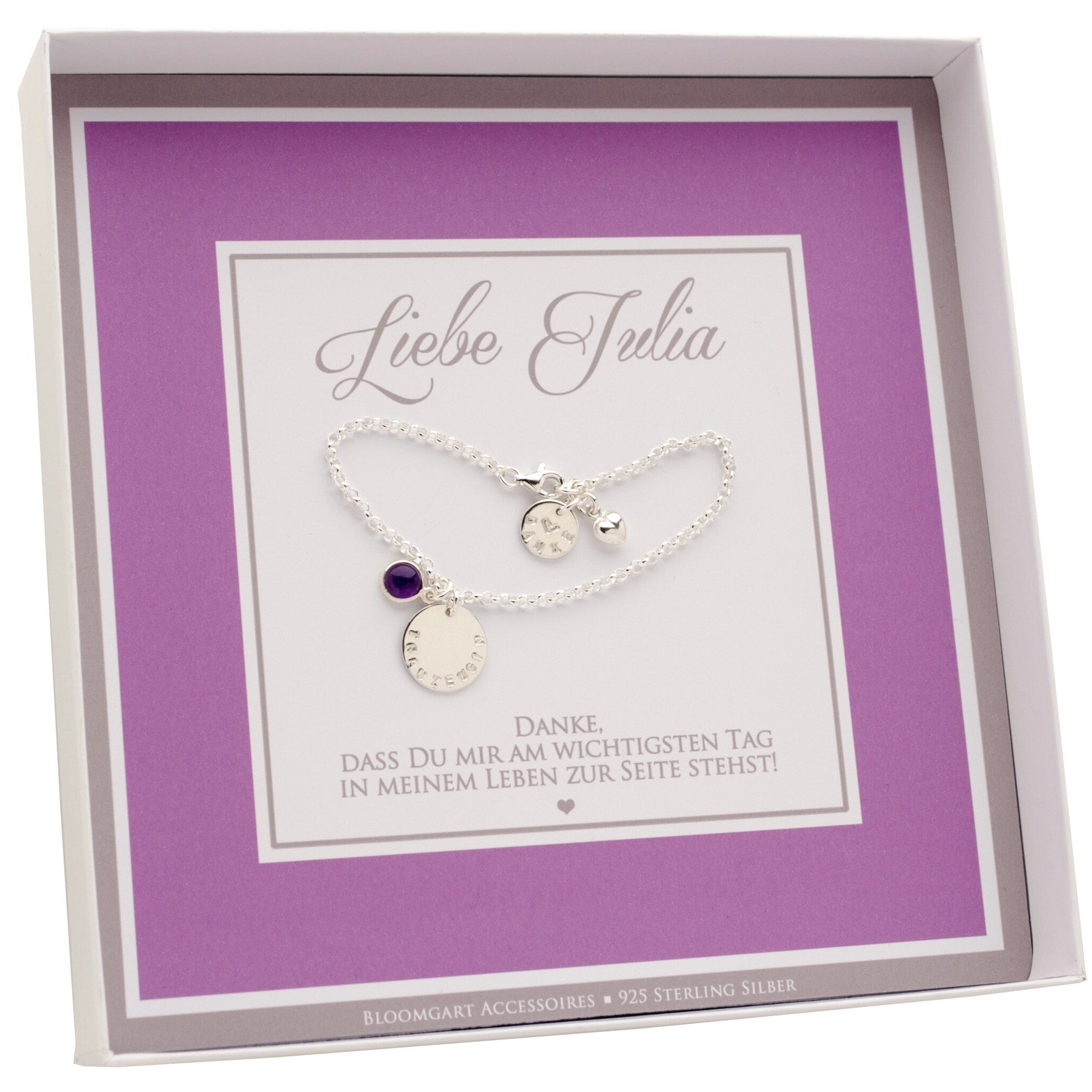 Innenansicht einer personalisierter Geschenkbox in flieder-grau-weiß mit der Aufschrift "Liebe Julia". Das Gliederarmband hat einen Amethyst-Anhänger, einen Gravurtaler "TRAUZEUGIN" und ein kleines Gravur-Plättchen am Verschluss "DANKE" mit Herz.