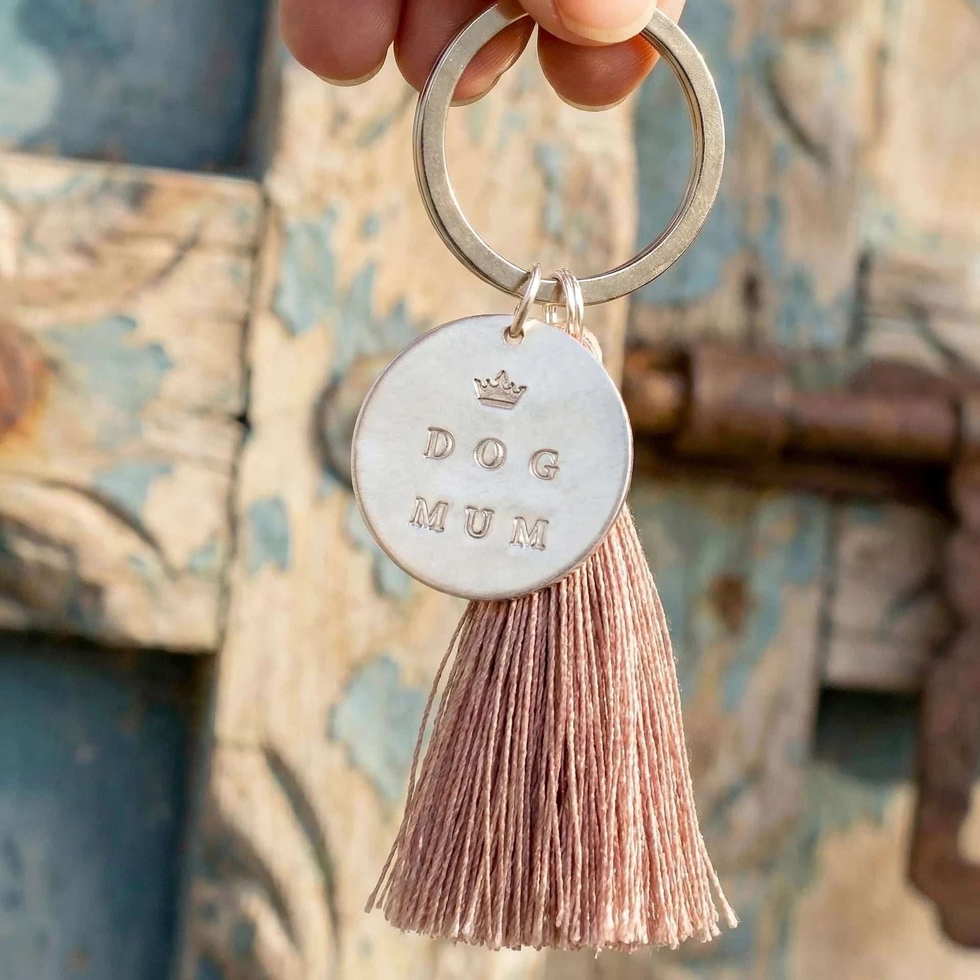 Ein handgestempelter Schlüsselanhänger mit Silbertaler 'DOG MUM' und Krone. Der Schlüsselring baumt an den Fingern einer Hand vor einer antiken Holztür.