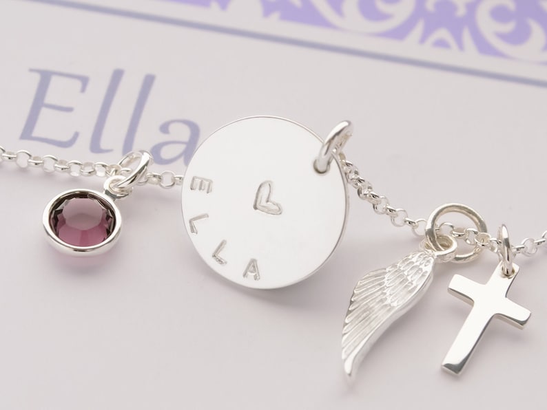 Detailansicht einer personalisierte Kette zur Kommunion für "Ella" aus 925 Silber mit Kreuz, Engelsflügel und Amethyst, präsentiert in einer lila Geschenkbox von Opa und Oma.
