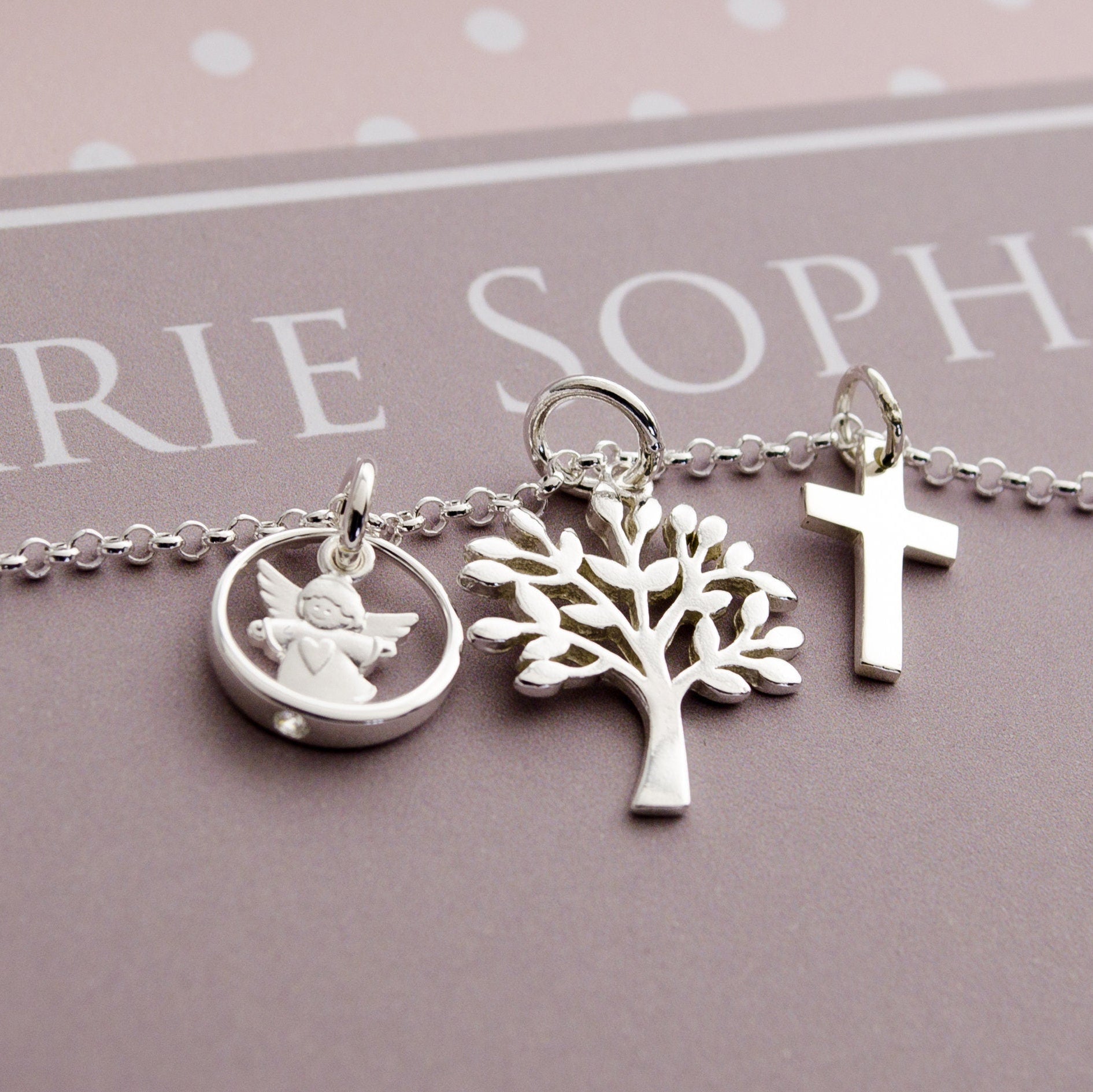 Nahansicht einer Kette mit Schutzengel im Taufring, Lebensbaum und Kreuz, fotografiert auf einer personalisierten Geschenkbox mit Namen.