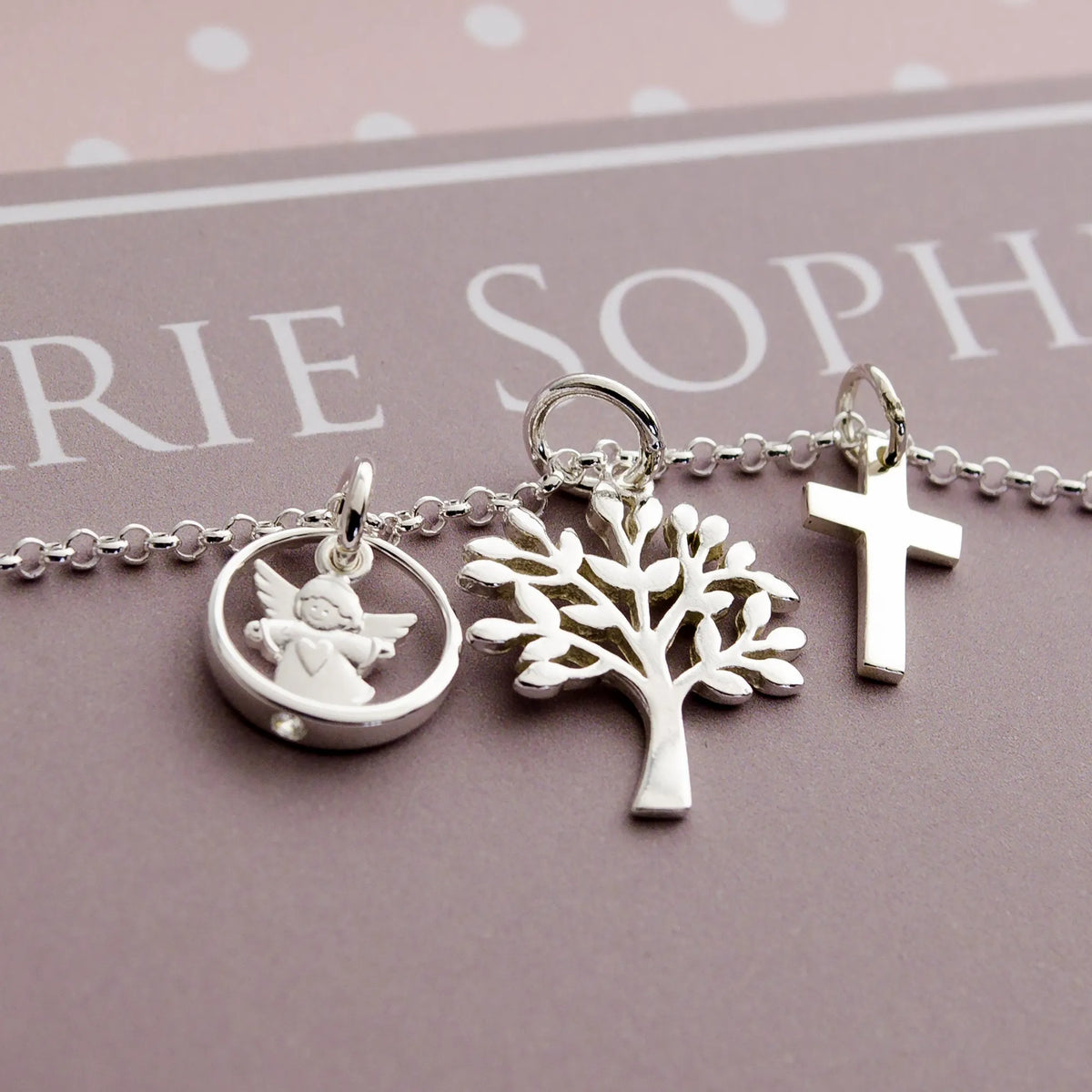 Detailansicht einer Kette mit Schutzengel im Taufring, Lebensbaum und Kreuz, fotografiert auf einer personalisierten Geschenkbox mit Namen.