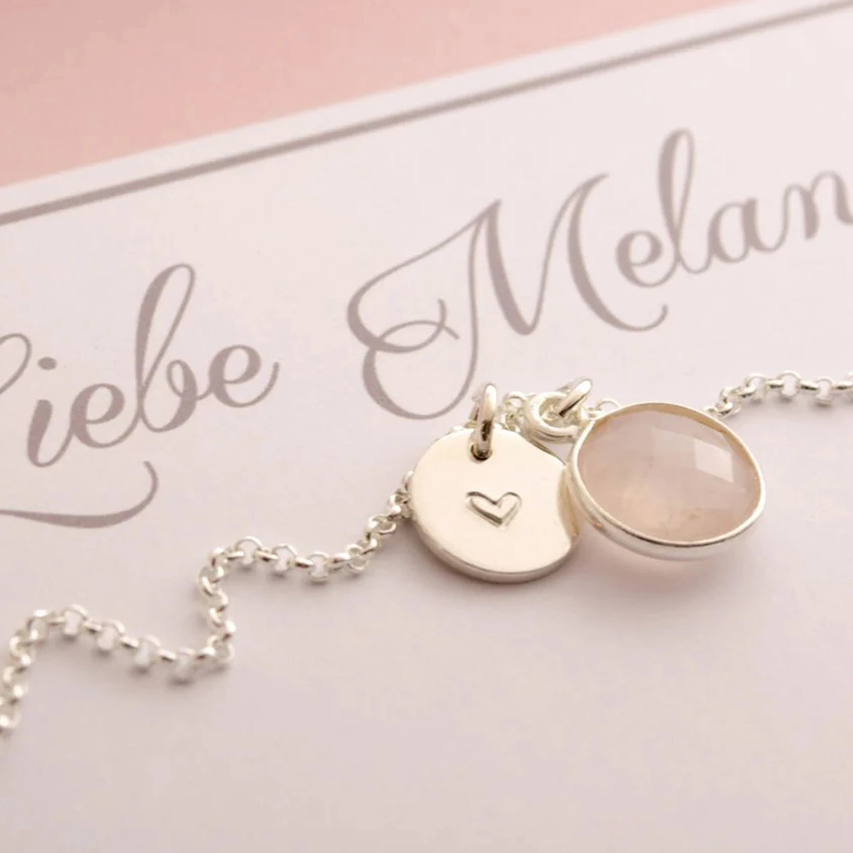 Feine Silberkette mit handgestempeltem Gravurtaler und Rosenquarz auf einer personalisierten weiß-rosa Karte.