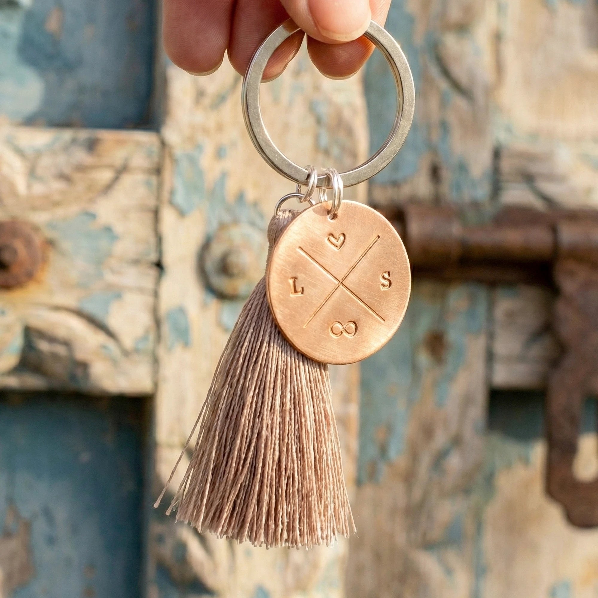 Personalisierter Schlüsselanhänger aus Kupfer mit Initialen, Herz und Unendlichkeitszeichen, handgestempelt, an einer Hand hängend für einer alten Tür.