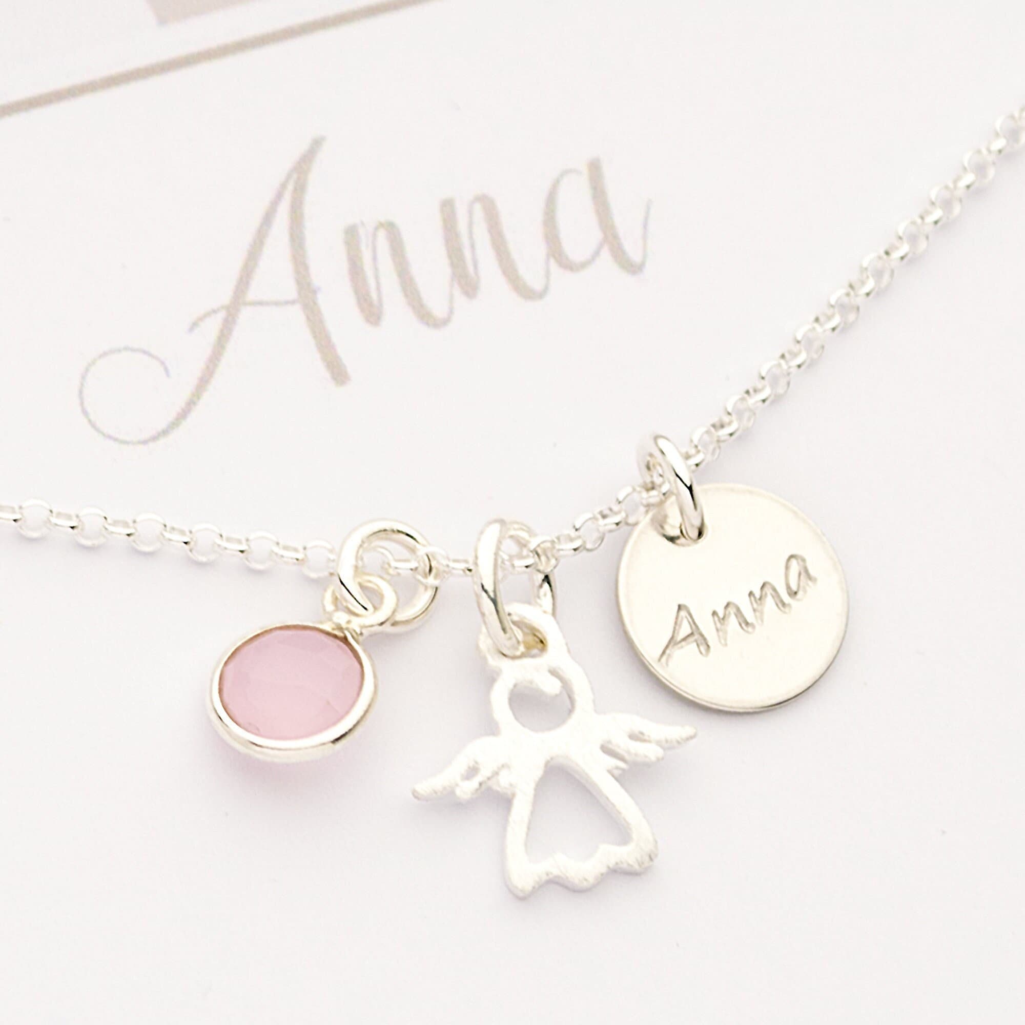 Nahaufnahme einer personalisierten Schutzengel-Kette aus 925 Silber. Mit einem filigranen Cutout-Engel, einem rosa Geburtsstein und einem Plättchen mit der Namensgravur 'Anna'. Von Bloomgart.