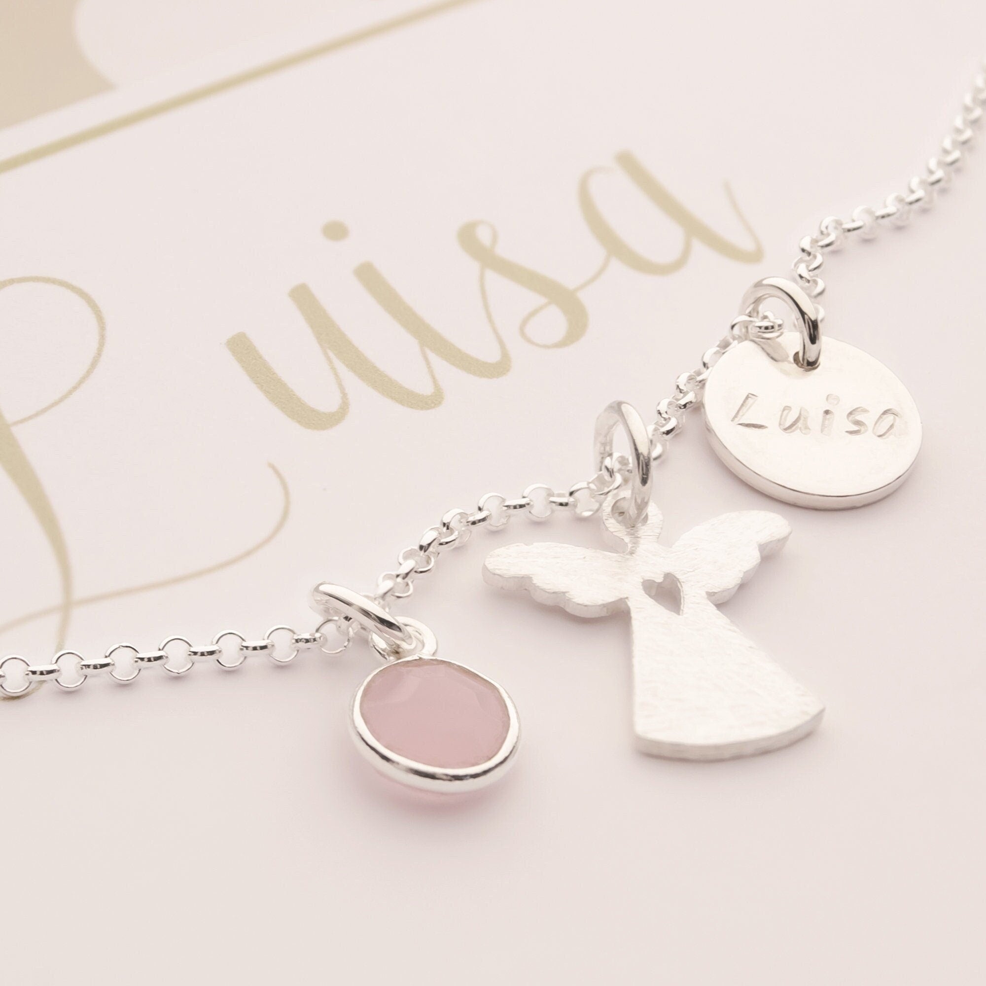 Nahaufnahme einer personalisierten Schutzengel-Kette aus 925 Silber. Mit einem filigranen Engel mit Herz Cutout, einem Rosenquarz und einem Plättchen mit der Namensgravur 'Luisa'. Von Bloomgart.