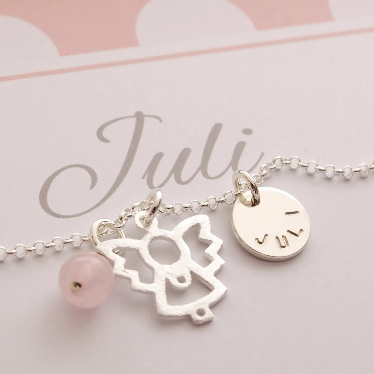 Detailansicht einer Silberkette mit Engel, Rosenquarzkugel und Namensanhänger in einer rosa-weiß gepunkteten, personalisierten Geschenkbox für 'Juli'.