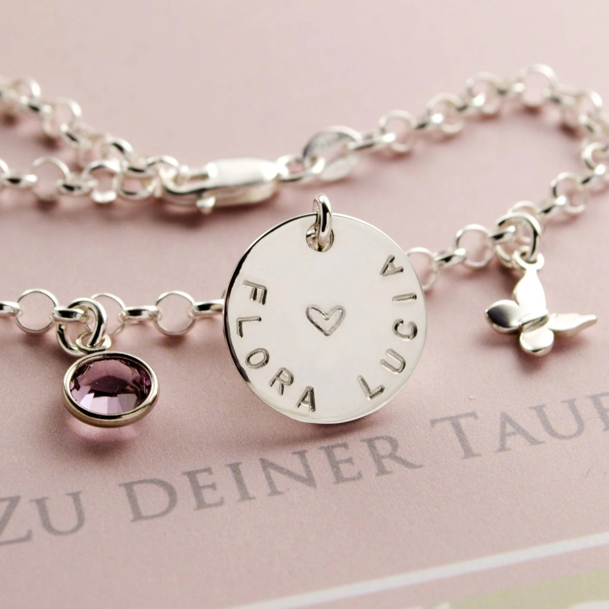 Zauberhaftes Namensarmband, personalisiert für 'FLORA LUCIA' mit Geburtsstein, großem Namensplättchen und Schmetterling.