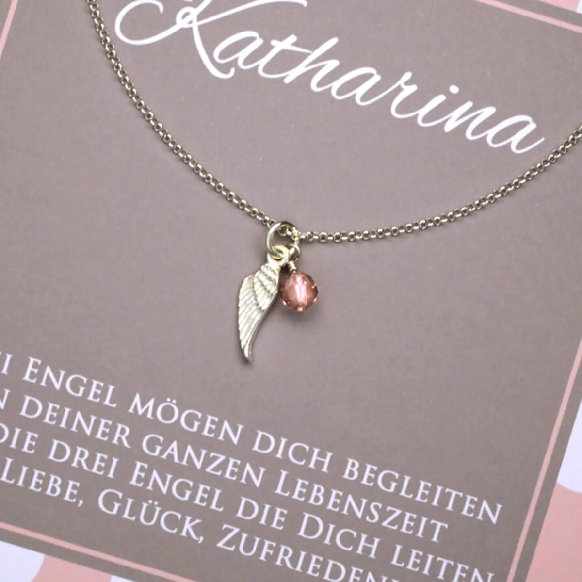 Detailansicht einer Silberkette mit Engelsflügel aus 925 Sterling Silber und rosa Glücksstein als Taufgeschenk fürs Patenkind, verpackt in einer personalisierten rosa-weiß gepunkteten Geschenkbox.