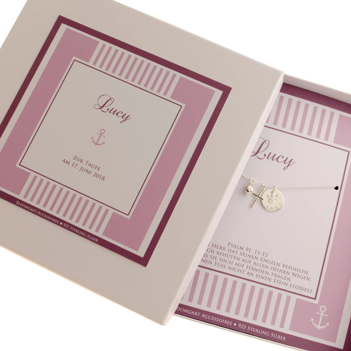 Gesamtansicht einer Geschenkbox mit Streifenmuster in dunkelrosa-Tönen, personalisiert für Lucy zur Taufe. In der Box befindet sind die 925 Silber Namenskette mit Schutzengel, Kreuz und Herz-Anhänger.
