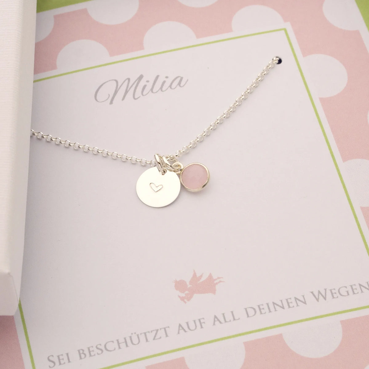 Makroaufnahme einer personalisierten Kette für Milia zur Einschulung mit Silbertaler und Rosenquarz in einer weiß-rosa Geschenkbox.