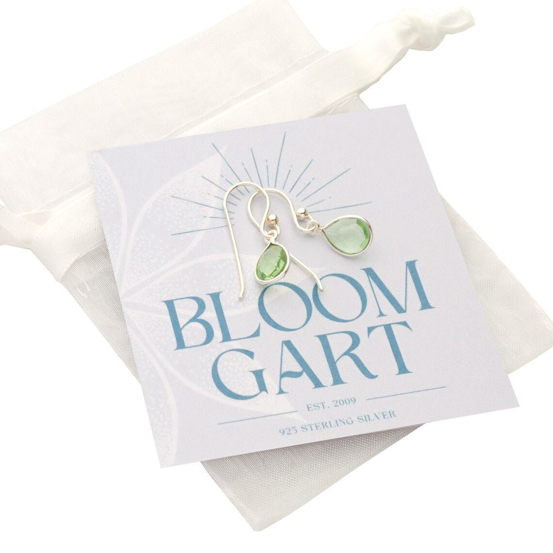 Zierliche Tropfen-Ohrringe mit grünen Amethysten in 925 Sterling Silber Fassungen auf einer blau-weißen Bloomgart Geschenkkarte montiert und in einem weißen Organza-Säckchen verpackt.